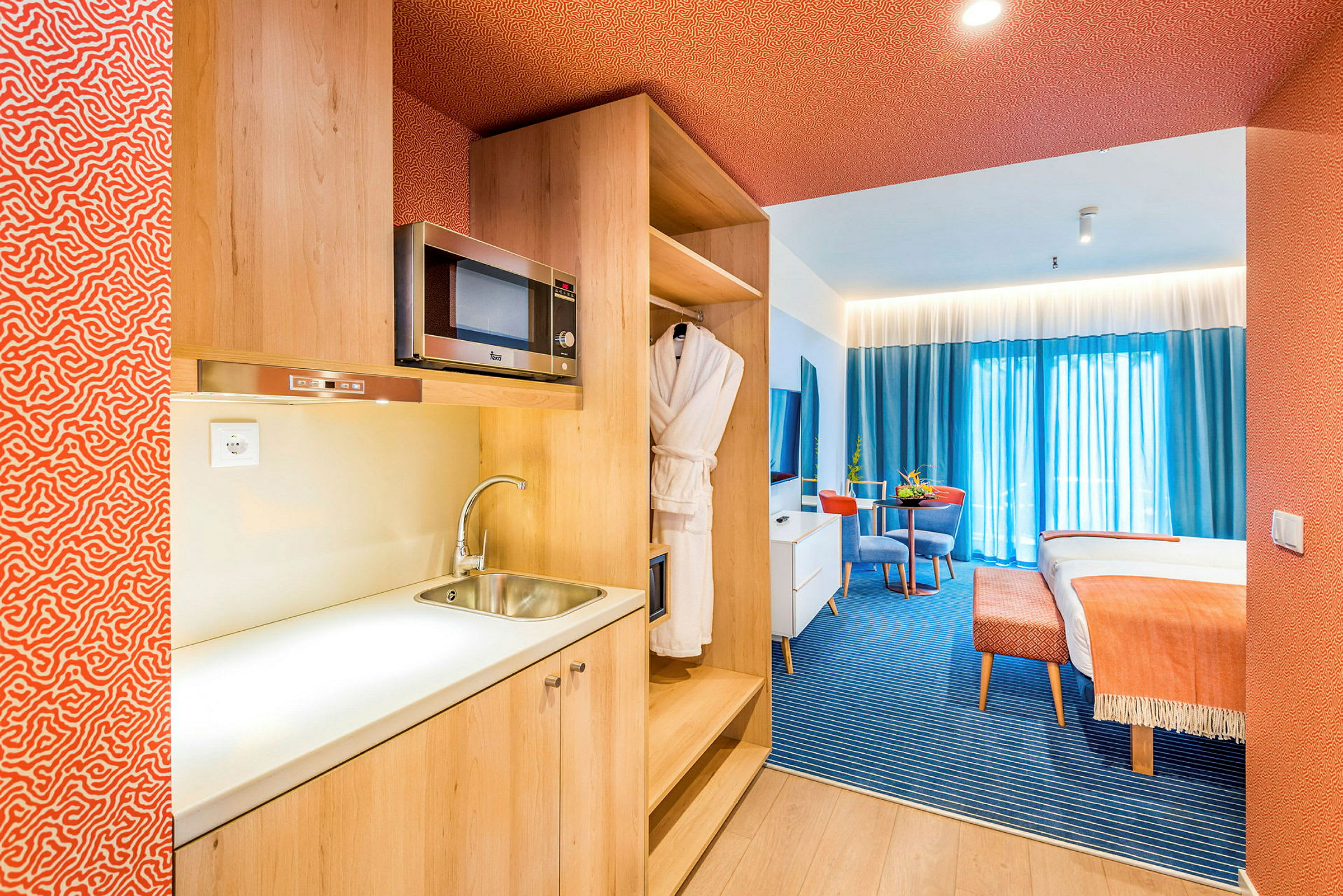 En hotelsuite med tekøkken, siddeområde og seng. (AI-genereret tekst)