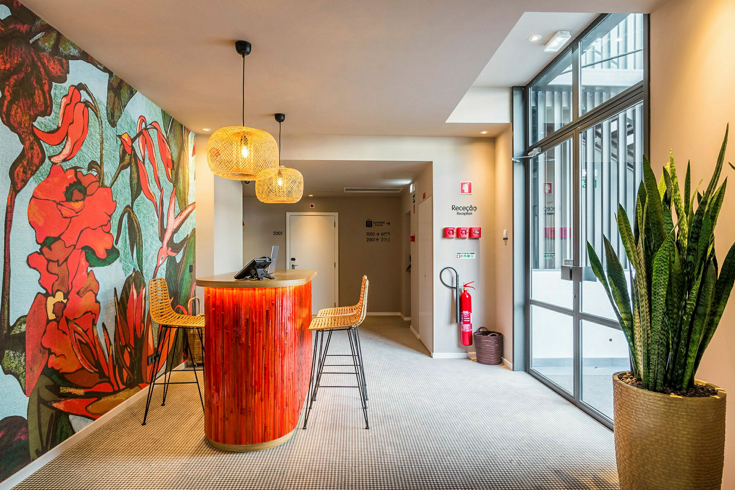 Reception med en dekorativ blomster væg, rød-orange reception og siddepladser med moderne lamper over. (AI-genereret tekst)