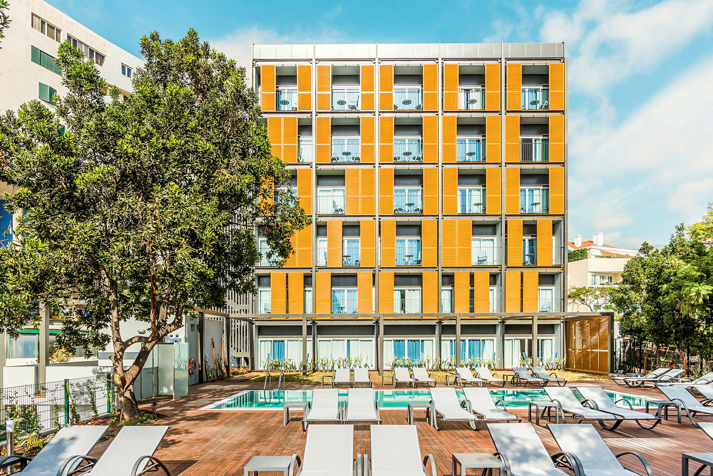 En bygning med orange facade ved en pool, omgivet af solsenge og træer. (AI-genereret tekst)