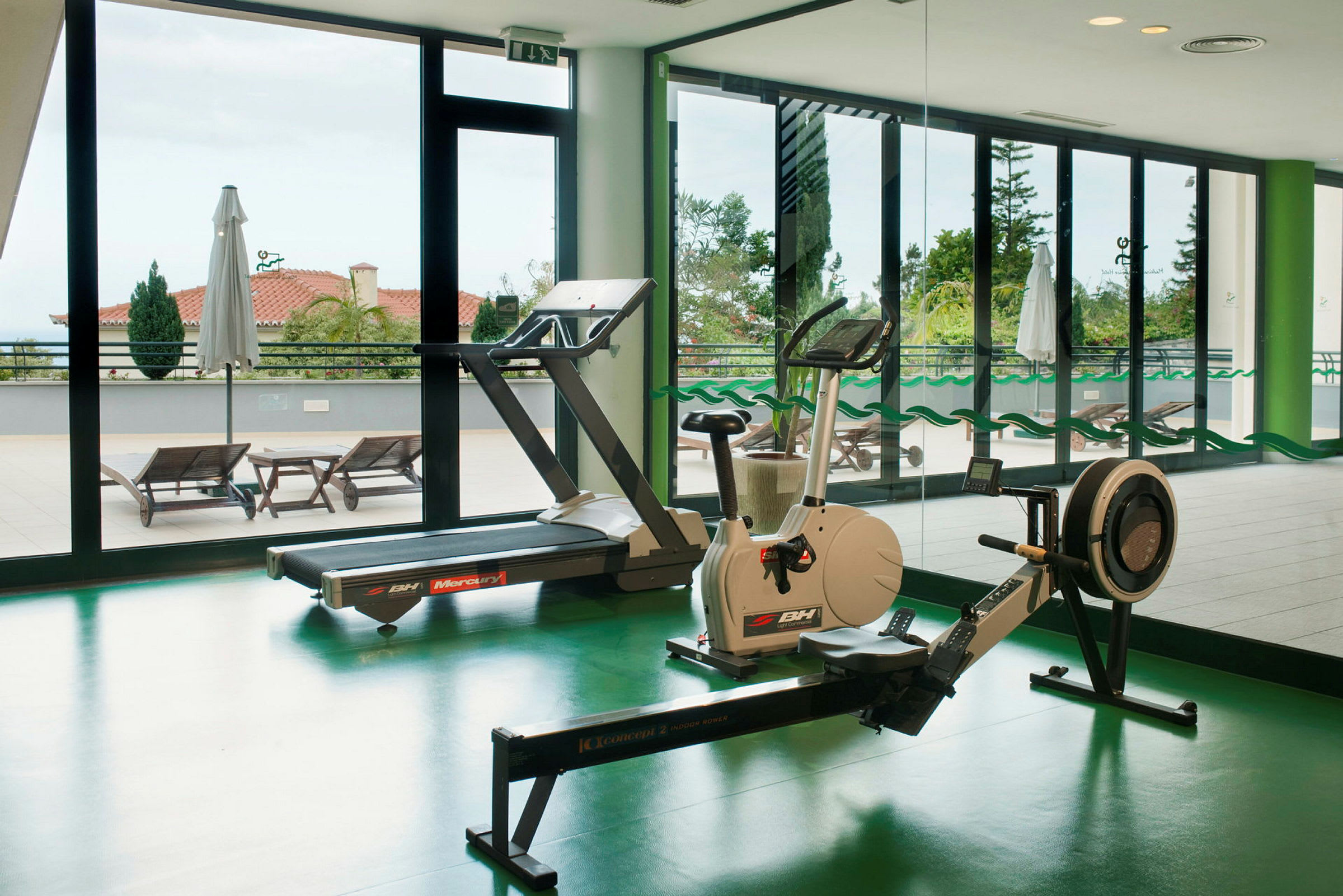Indendørs fitnesscenter med træningsudstyr foran store vinduer. (AI-genereret tekst)