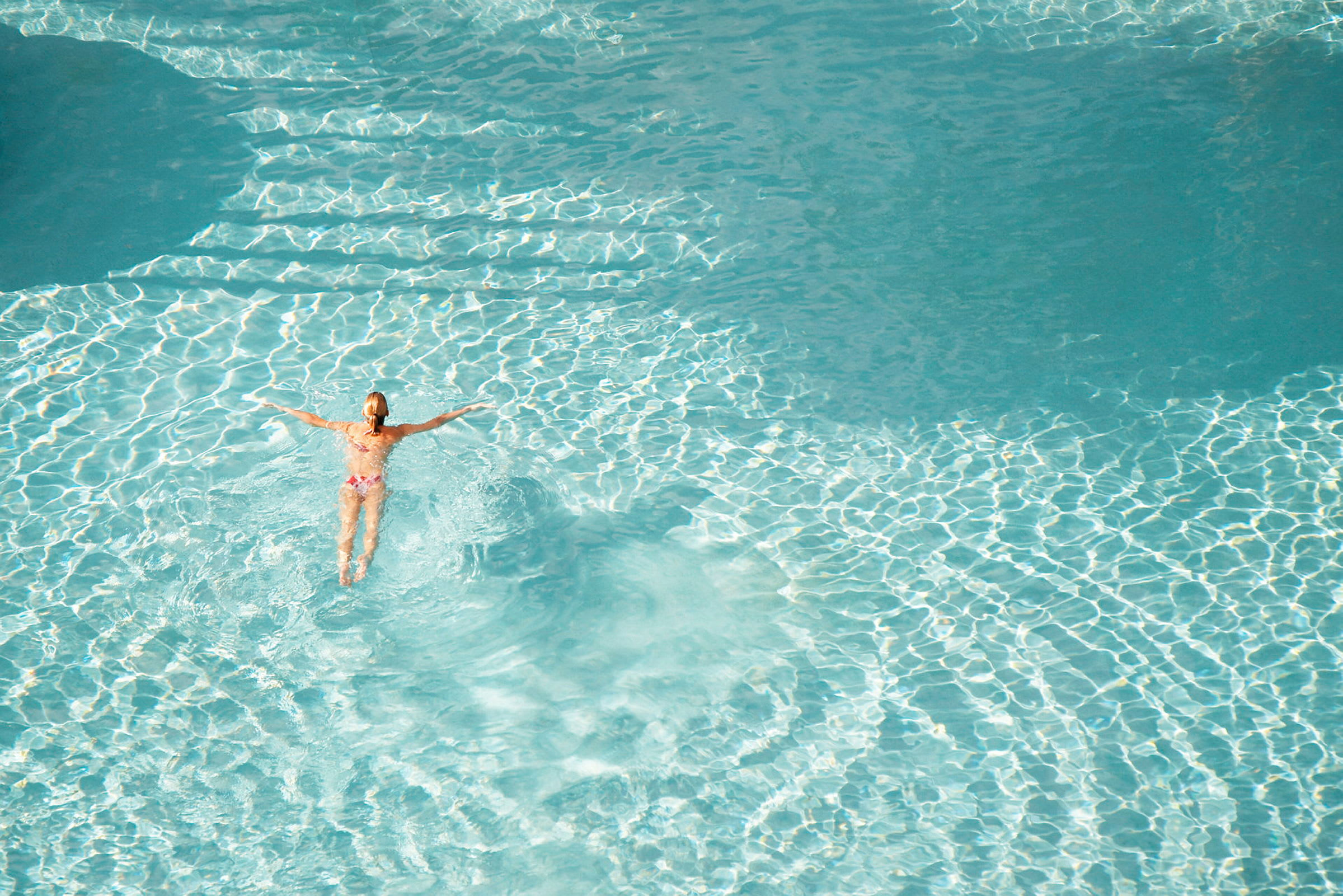En person svømmer i en klarblå pool. (AI-genereret tekst)