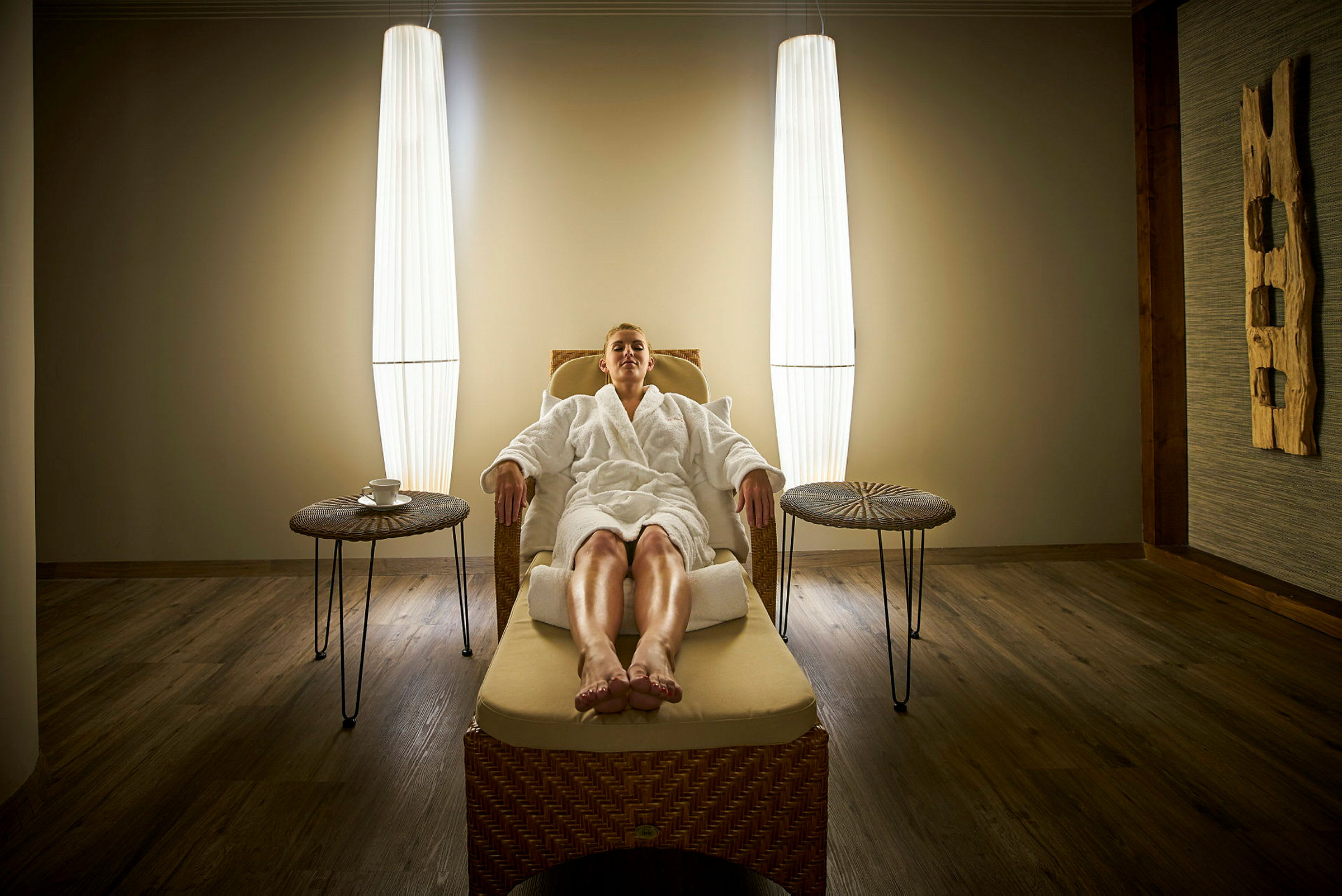 En person sidder afslappet i en spa-lounge i en stol af flet, omgivet af blød belysning. (AI-genereret tekst)