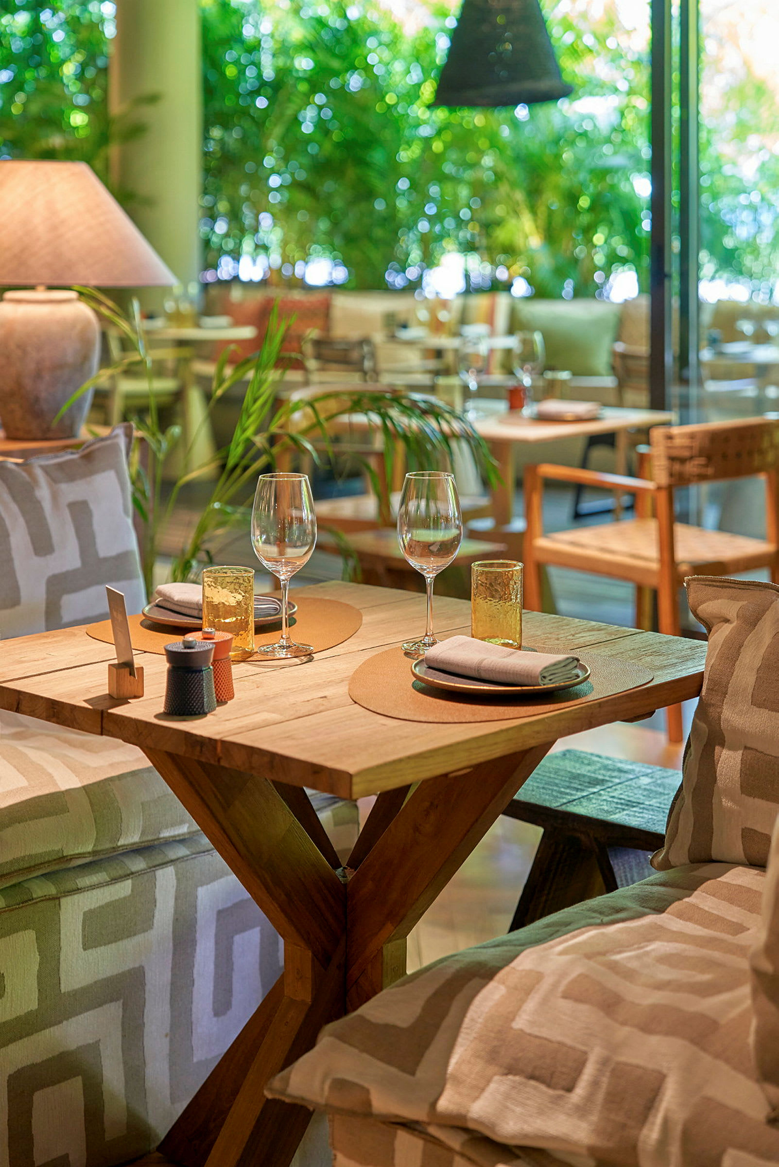 Et dækket bord med tallerkener, vinglas og servietter i en restaurant med frodig baggrund. (AI-genereret tekst)