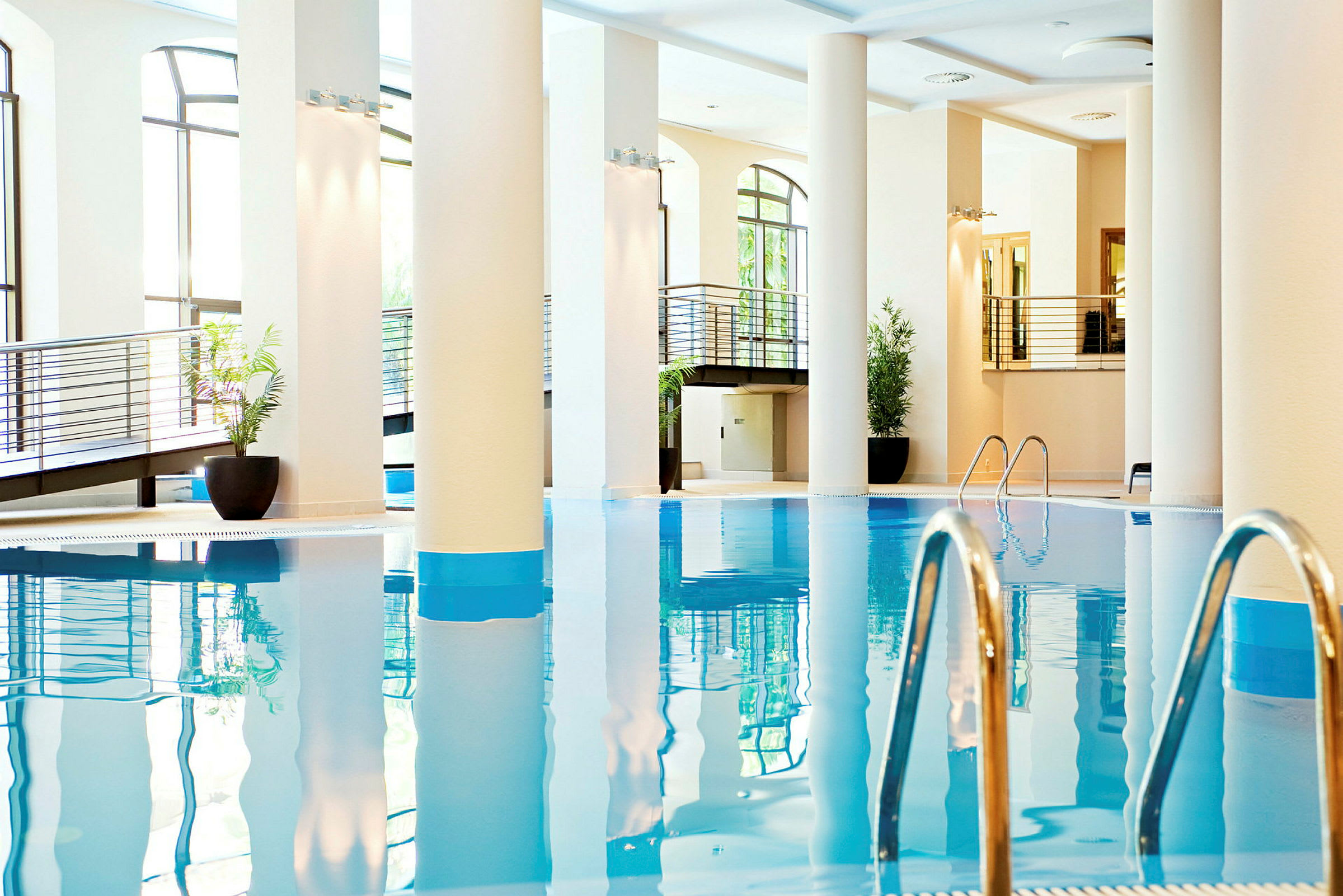En indendørs swimmingpool med metalstiger og omkringliggende moderne arkitektur. (AI-genereret tekst)