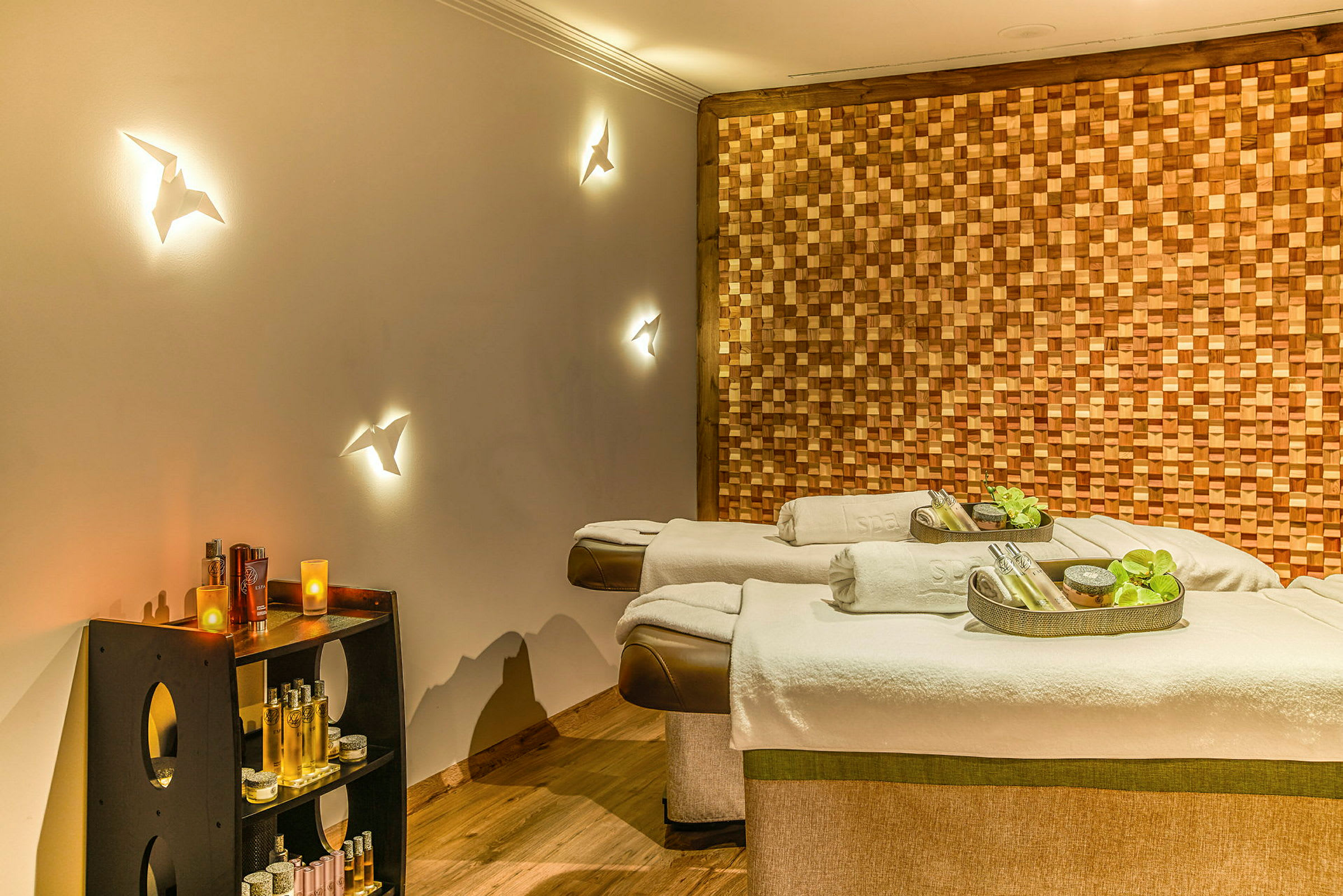 To spa-massageborde med dekorative tilbehør, omgivet af en vægpanel af træ og hylder med forskellige spa-produkter. (AI-genereret tekst)