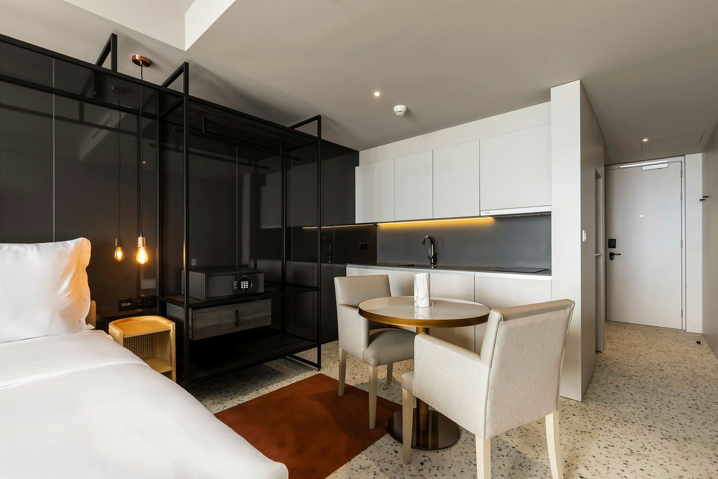 Et moderne hotelværelse med åben planløsning, der inkluderer en dobbeltseng, køkken og spisebord. (AI-genereret tekst)