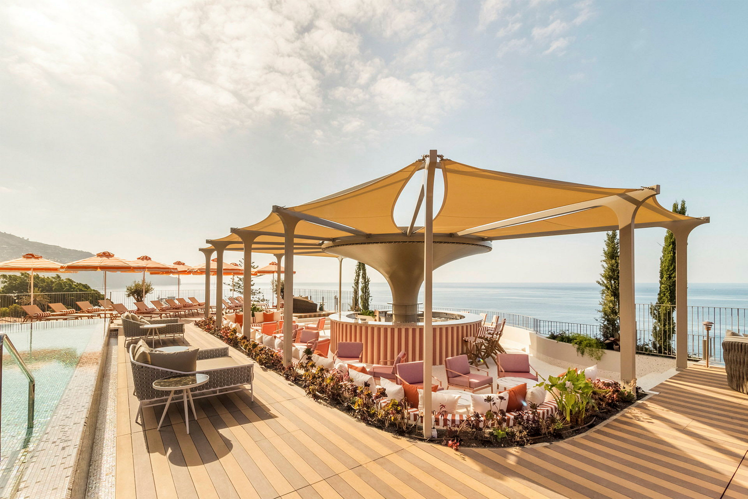 En terrasse med pool, liggestole, parasoller og siddepladser under et skyggefuldt tag. Udsigt over havet. (AI-genereret tekst)