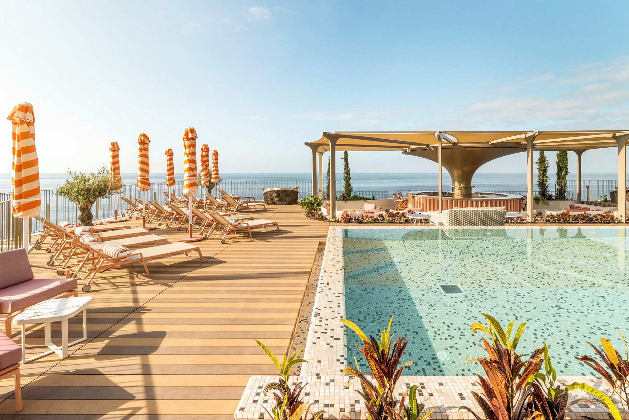 En pool med mosaik ved en træterrasse med liggestole og orange-hvide parasoller. (AI-genereret tekst)