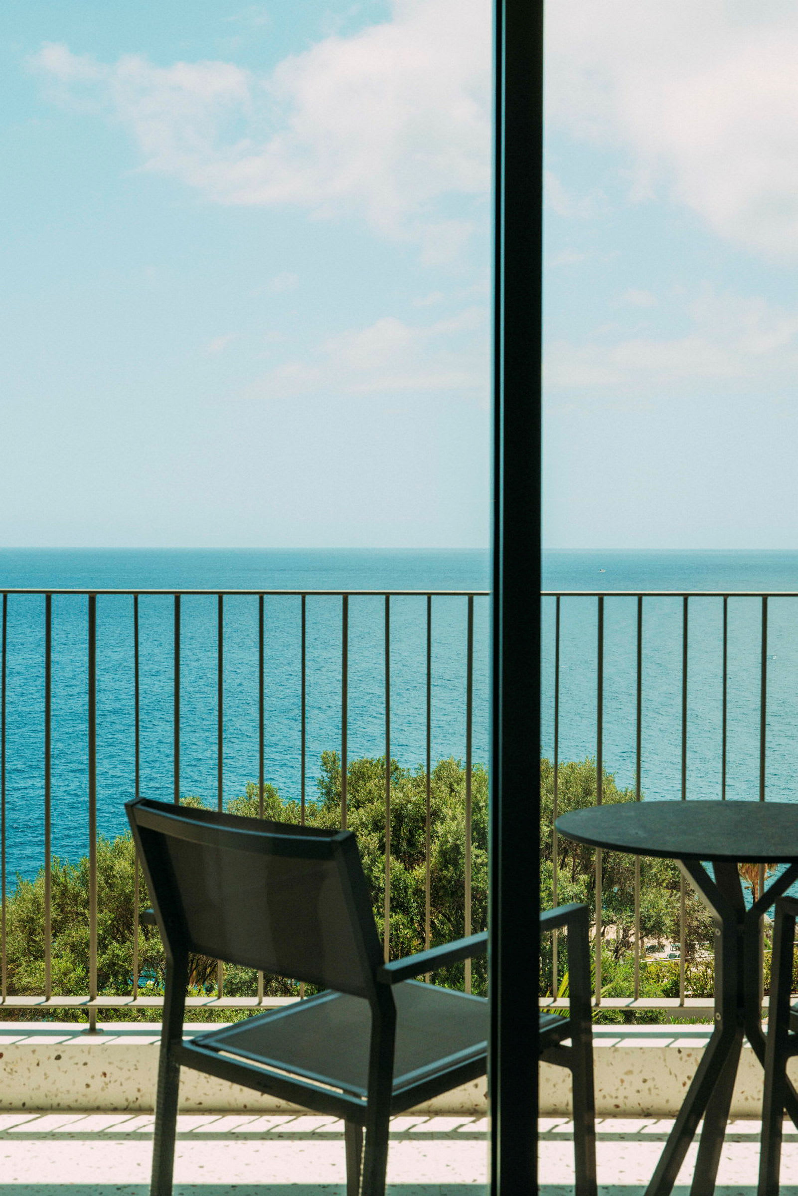 Udsigt over havet fra en balkon med et bord og en stol. (AI-genereret tekst)