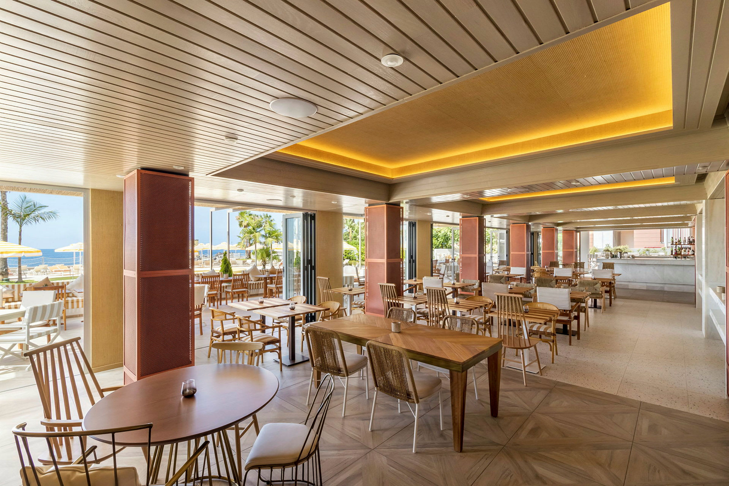 En moderne restaurant med træborde og stole, åben ud mod udendørsmiljø med palmer. (AI-genereret tekst)
