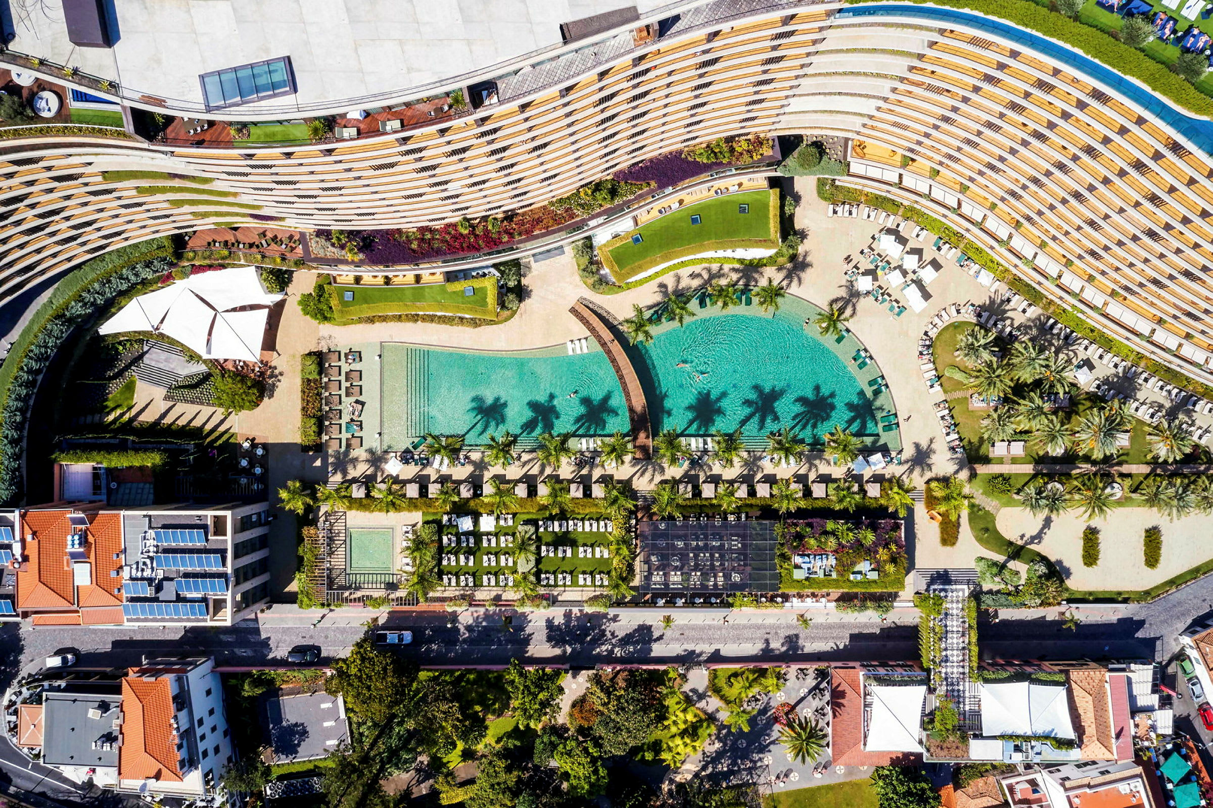 Luftfoto af et hotelområde med pool, liggestole og have. (AI-genereret tekst)