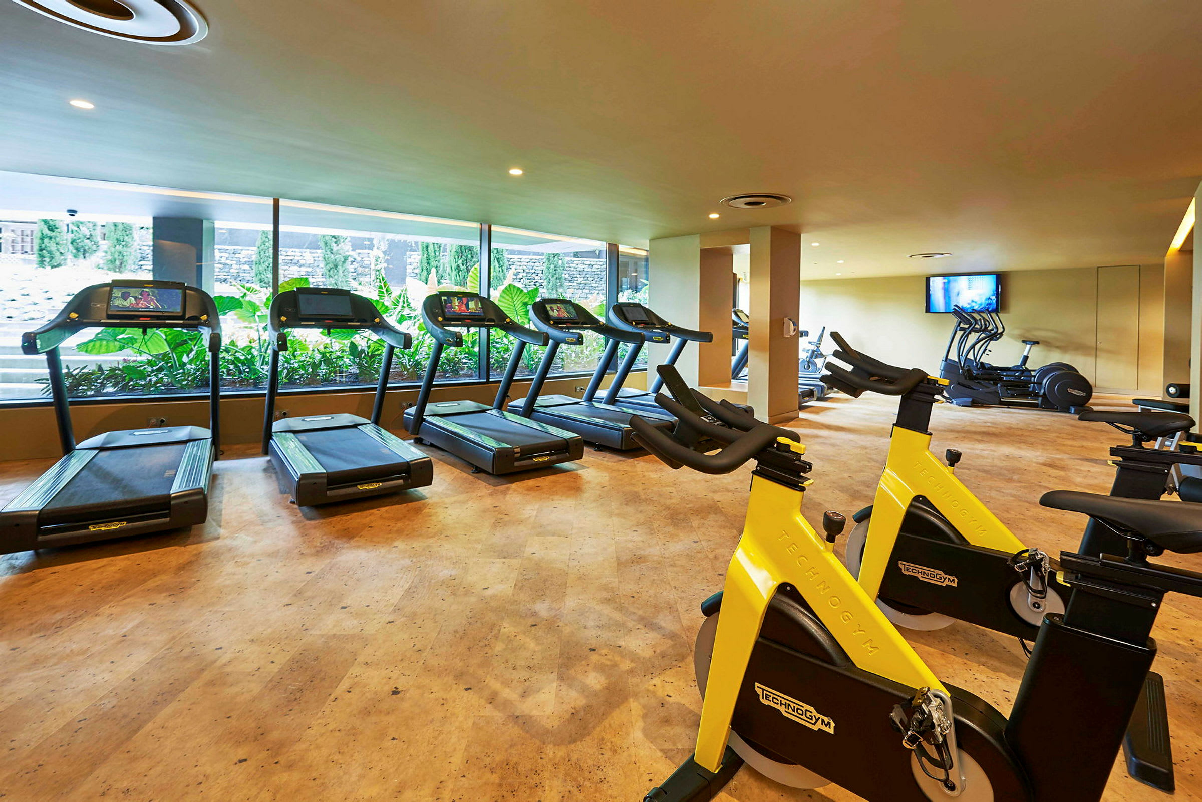 Fitnessrum med løbebånd og motionscykler foran store vinduer. (AI-genereret tekst)