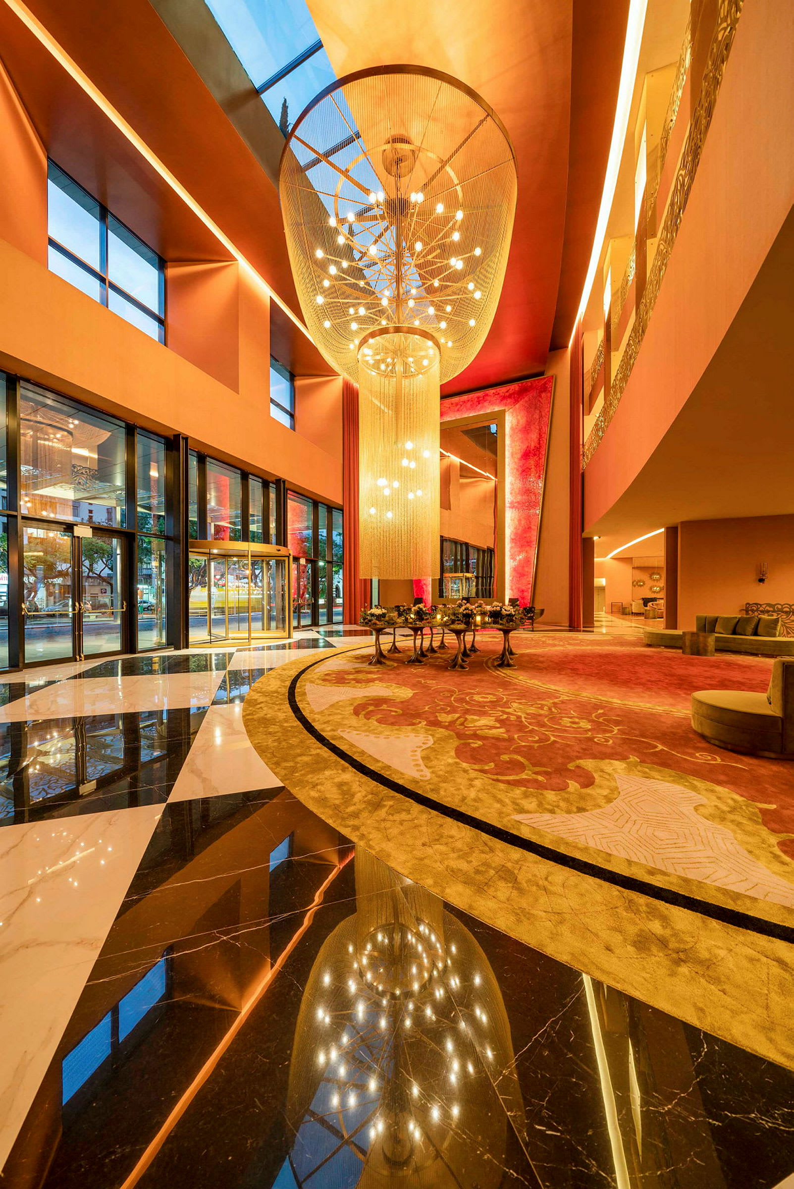 En hotellets foyer med store vinduer, farverige tæpper og en stor lysekrone. (AI-genereret tekst)