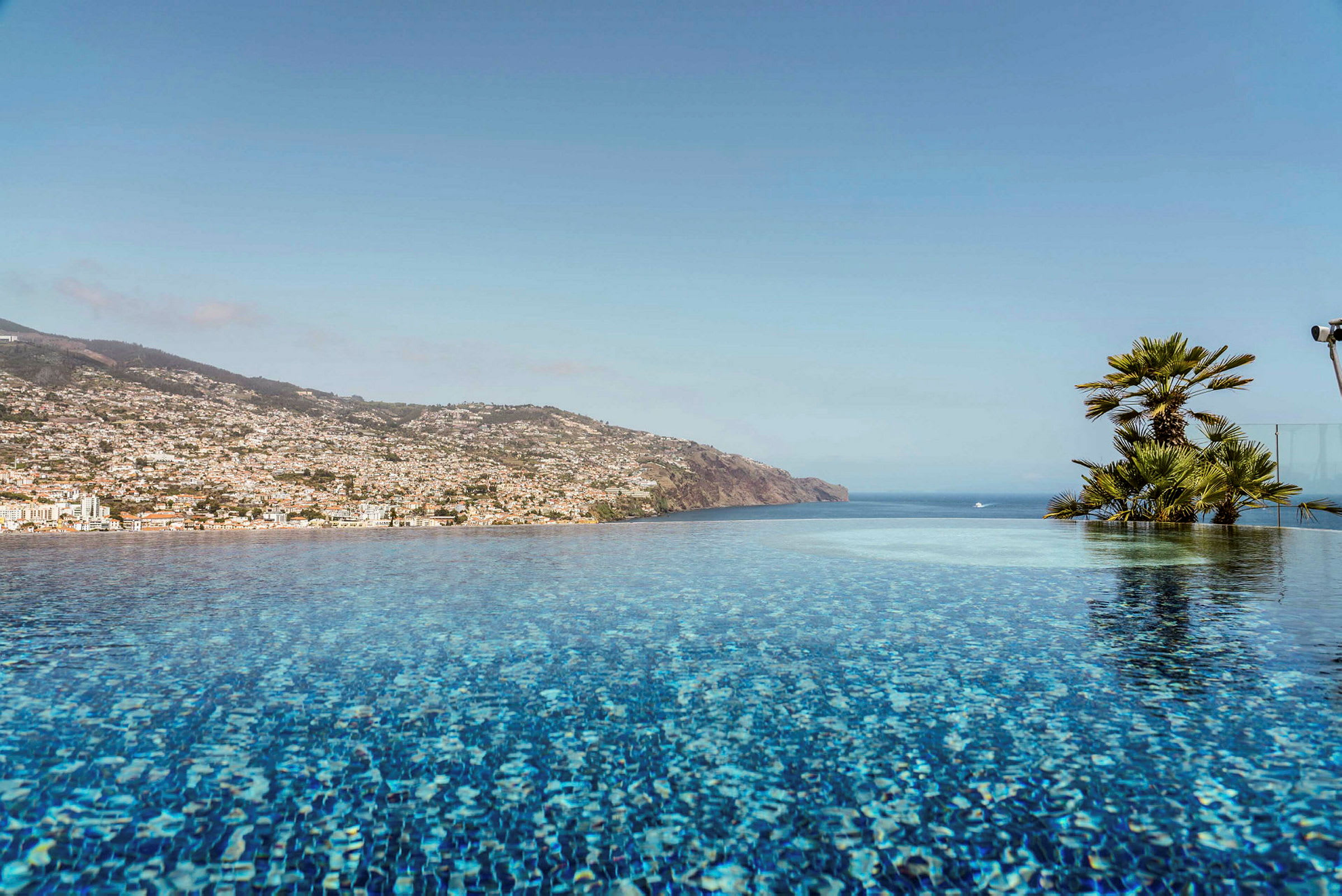 En infinitypool med udsigt over havet og en bjergskråning fyldt med bygninger. (AI-genereret tekst)