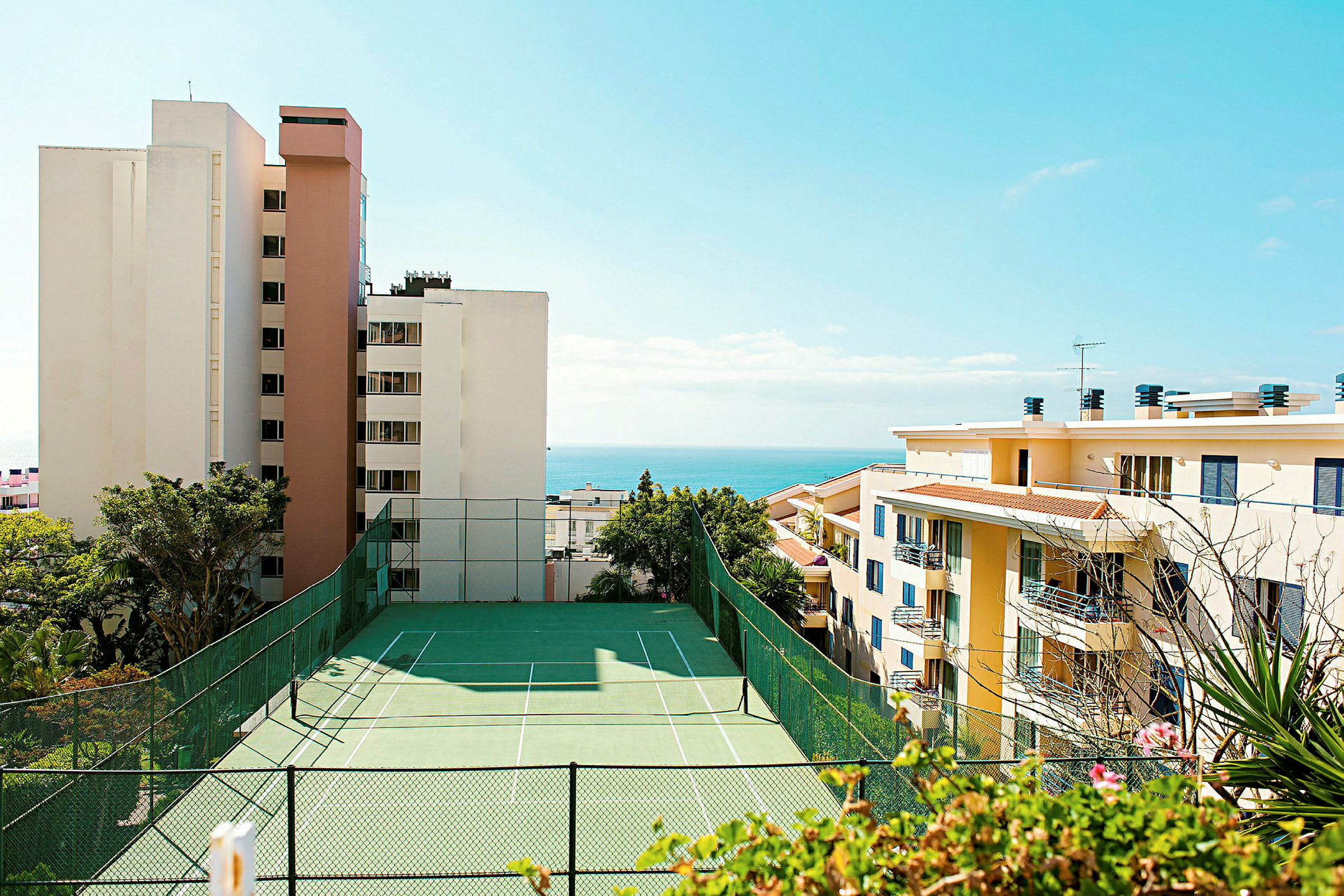 Udsigt over tennisbane med høje bygninger og havet i baggrunden. (AI-genereret tekst)
