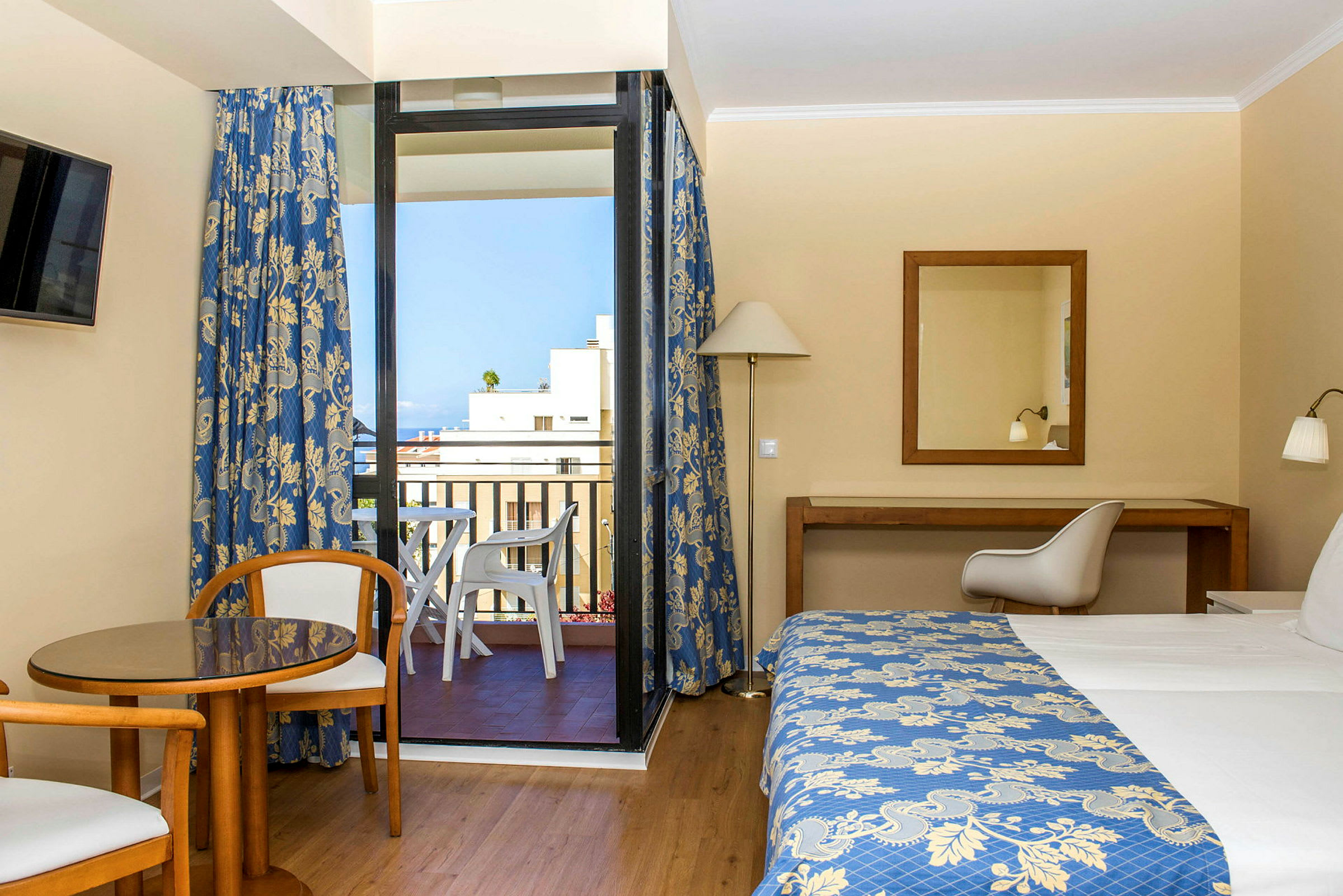 Hotelværelse med en seng, et bord og to stole samt en altan med udsigt. (AI-genereret tekst)