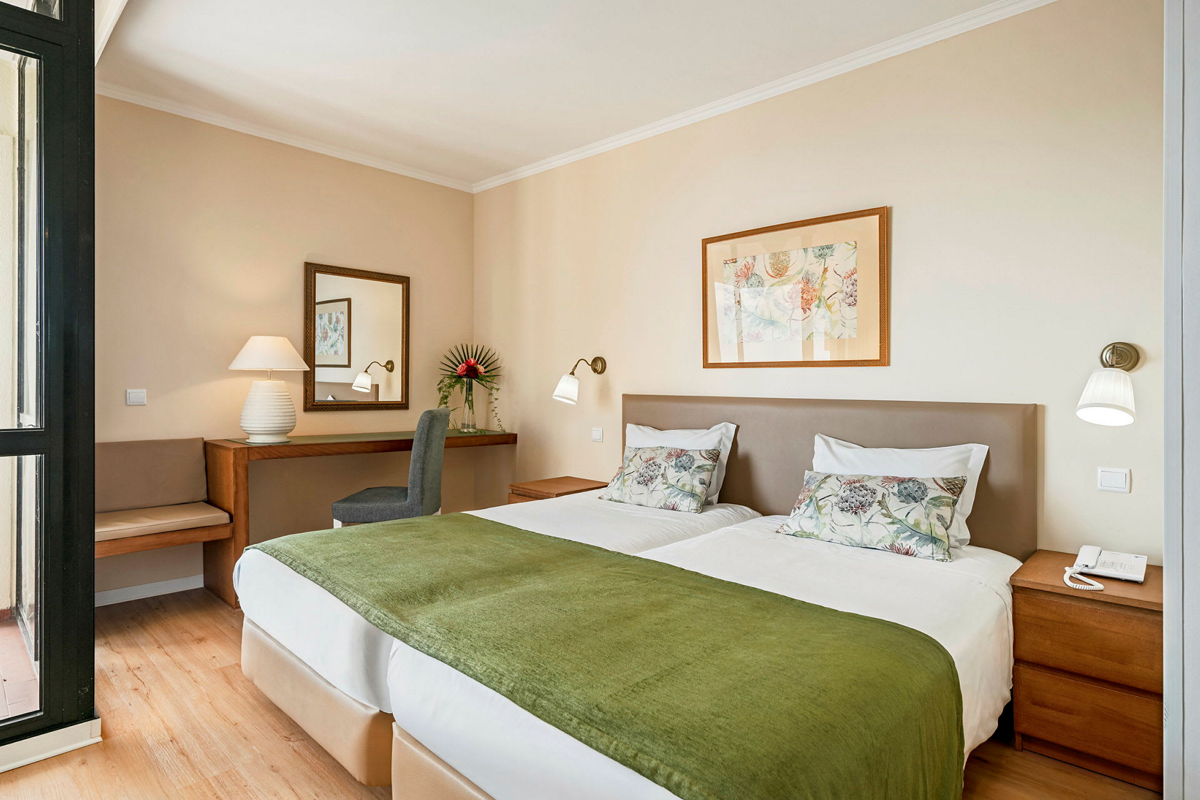 Billede af et hotelværelse med to enkeltsenge med hvidt sengetøj og grønne tæpper, et skrivebord med spejl og en stol i baggrunden. (AI-genereret tekst)