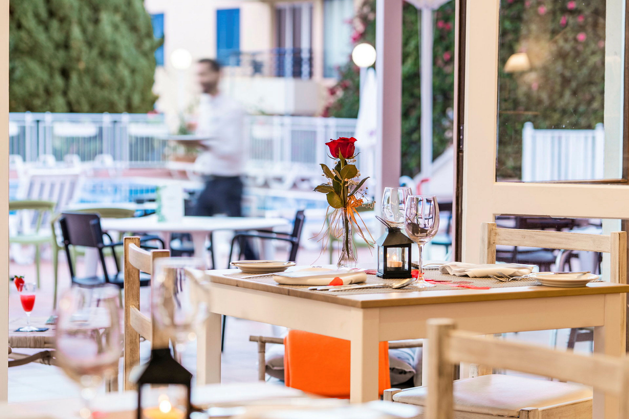 Udendørs servering med et dækket bord med en rose i vase, glas og borddækning. (AI-genereret tekst)