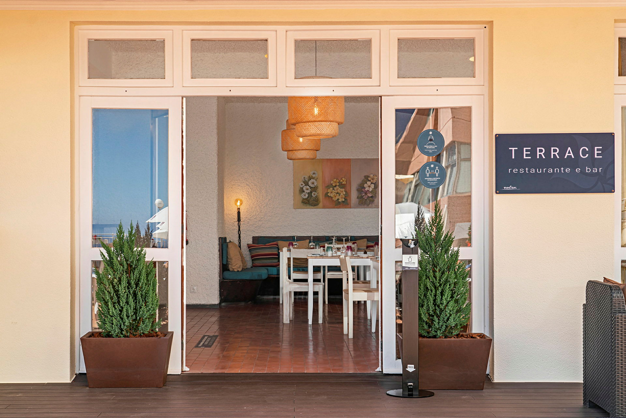 Indgangen til en restaurant med navnet Terrace, indenfor ses borde og stole samt dekorerede vægge. (AI-genereret tekst)