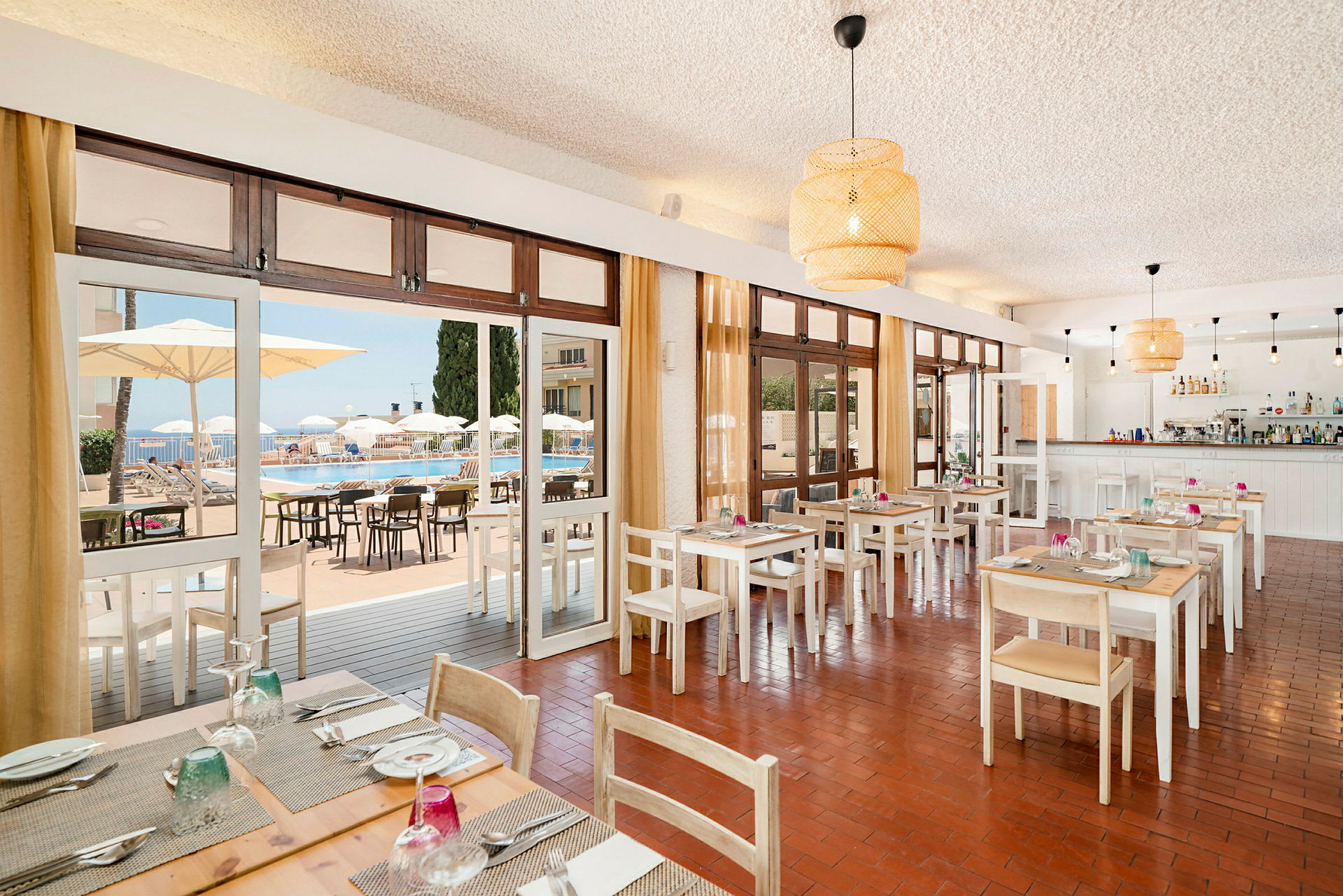 En restaurant med dækkede borde og udsigt til en pool gennem glasdøre. (AI-genereret tekst)