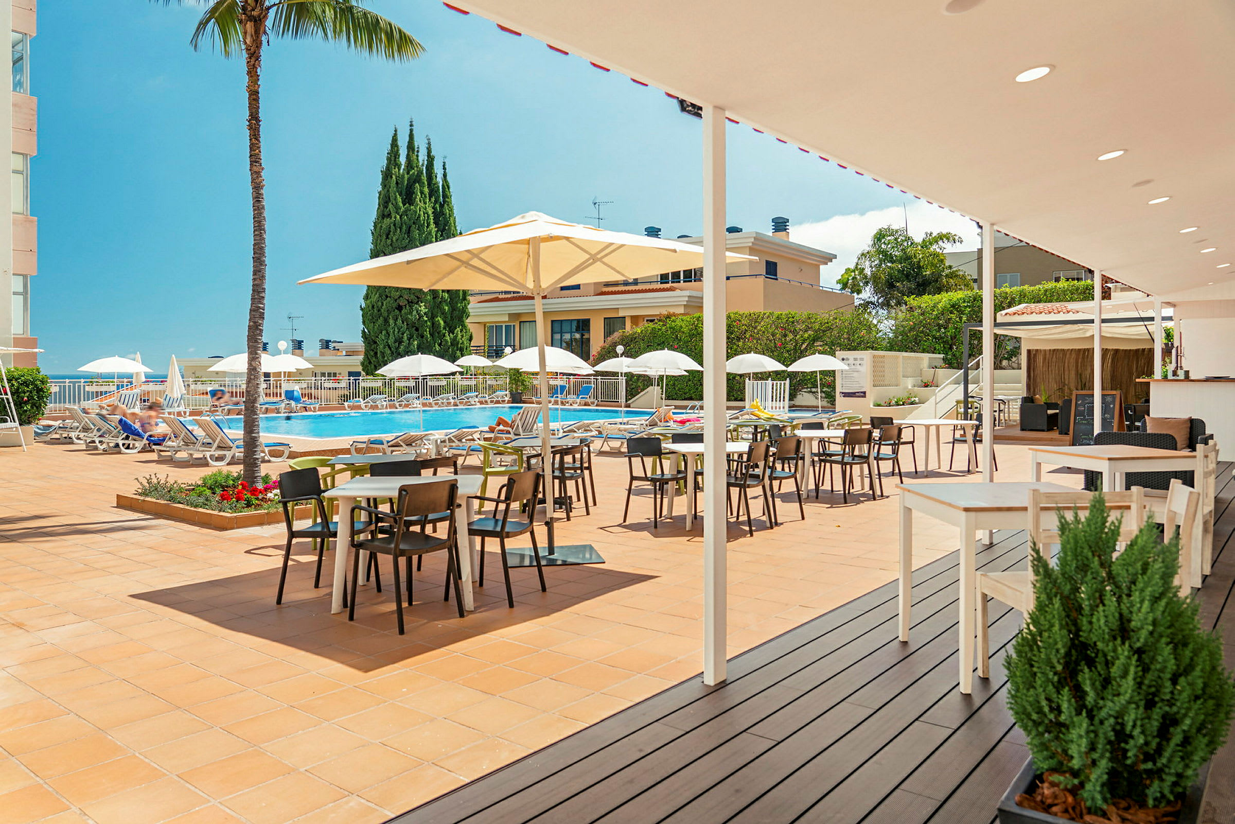 Billede af en solrig terrasse med borde og stole nær en pool. (AI-genereret tekst)