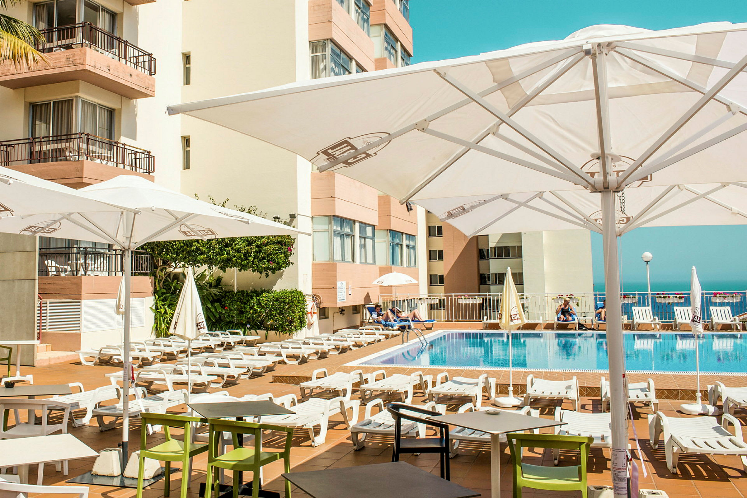 Udendørs poolområde med liggestole og parasoller ved et hotel. (AI-genereret tekst)