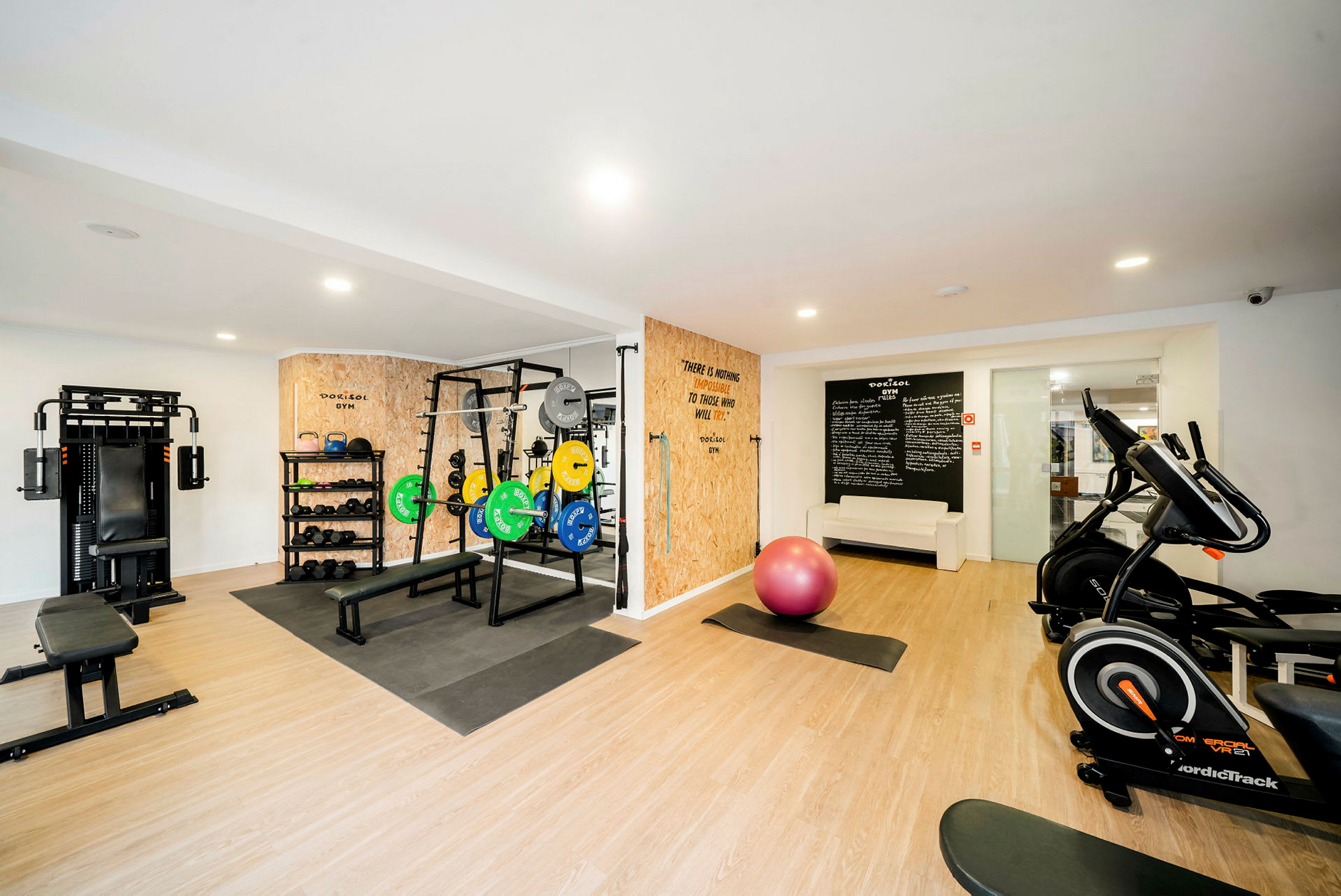 Et fitnesscenter med træningsmaskiner, vægte og en lyserød balancebold. (AI-genereret tekst)