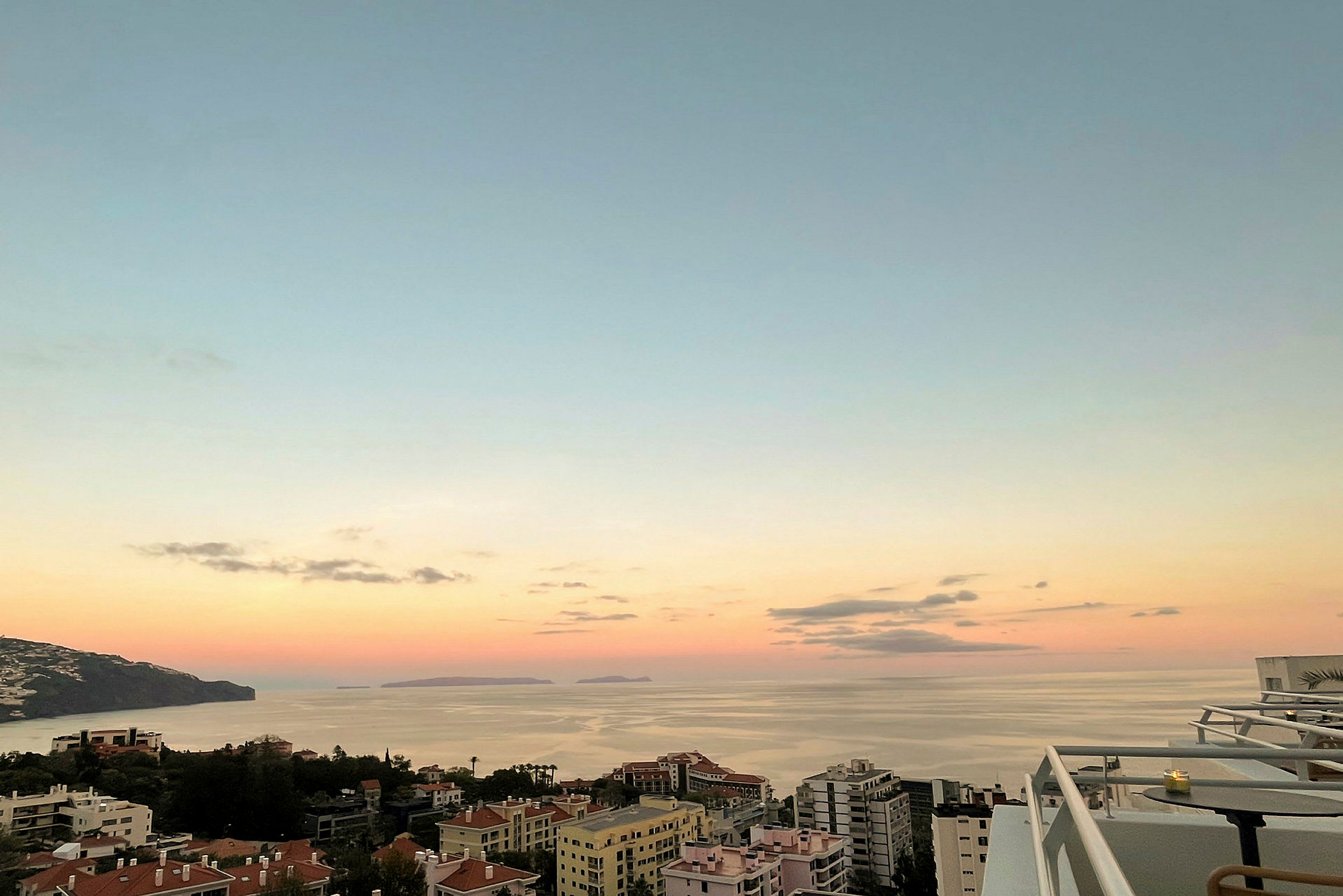 Billede af en kystby med bygninger i forgrunden og havet i baggrunden ved solnedgang. (AI-genereret tekst)