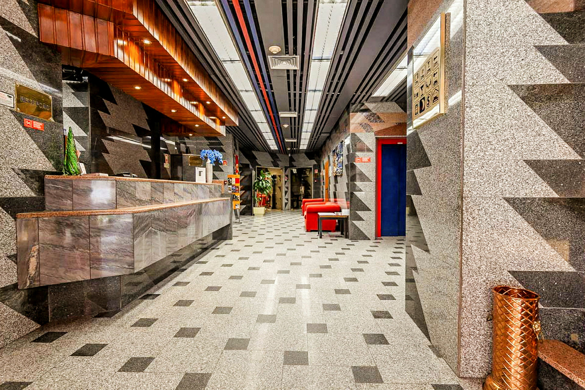 Hotellets lobby med marmorindretning, et receptionsområde og røde siddemøbler. (AI-genereret tekst)