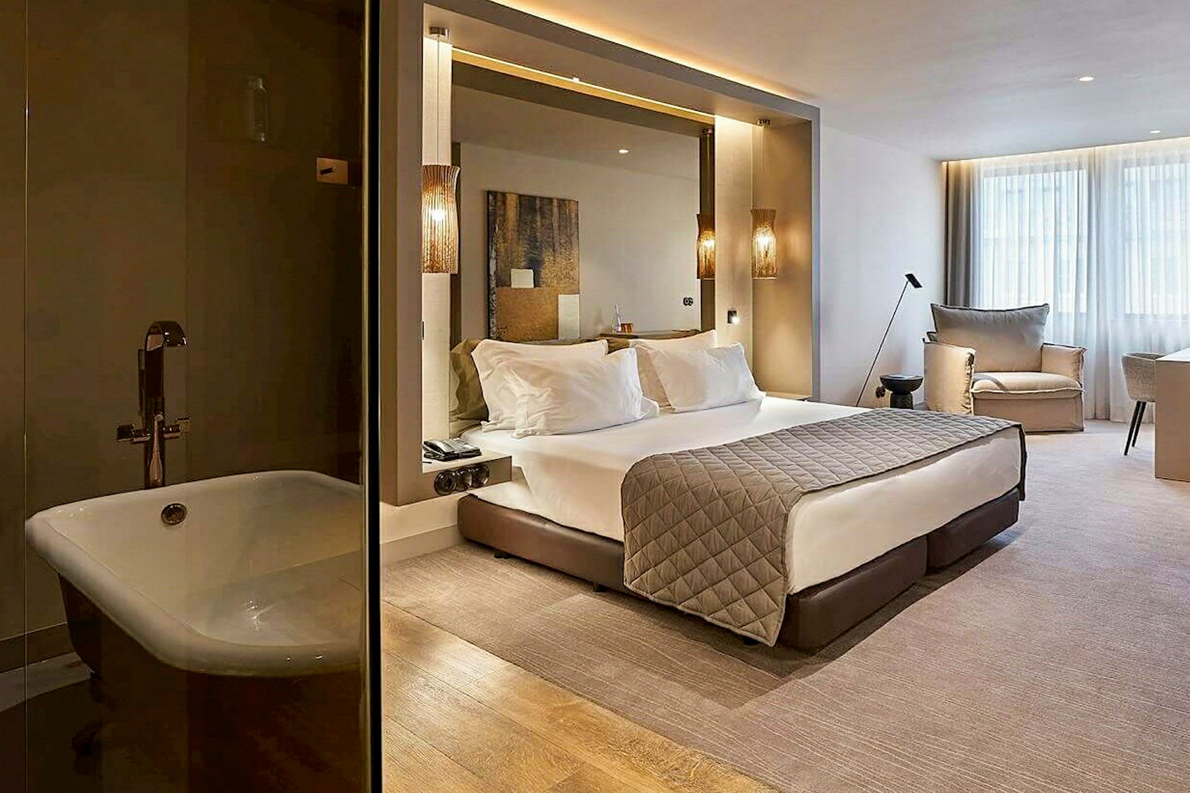 Et moderne hotelværelse med en stor seng, siddeområder og vinduer. Til venstre ses et badekar. (AI-genereret tekst)