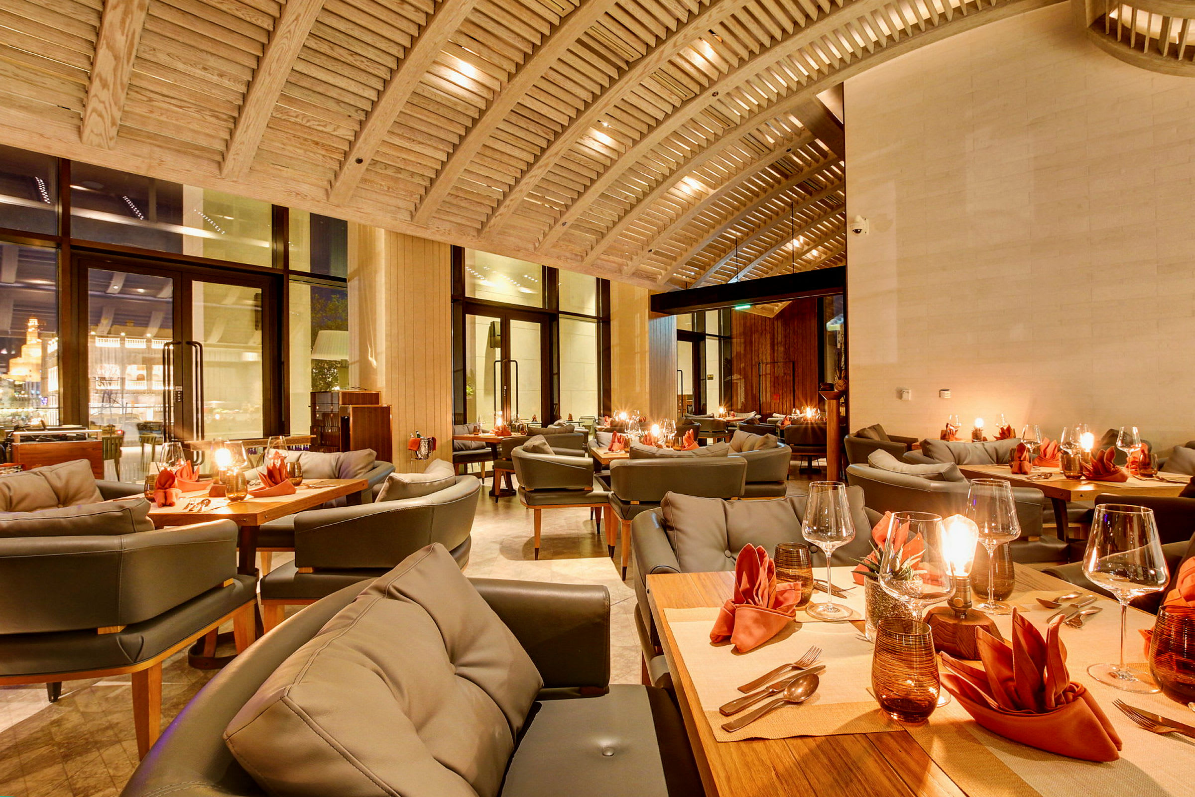 En elegant restaurant med bjælkeloft, dækkede borde med orange servietter og hyggelig belysning. (AI-genereret tekst)