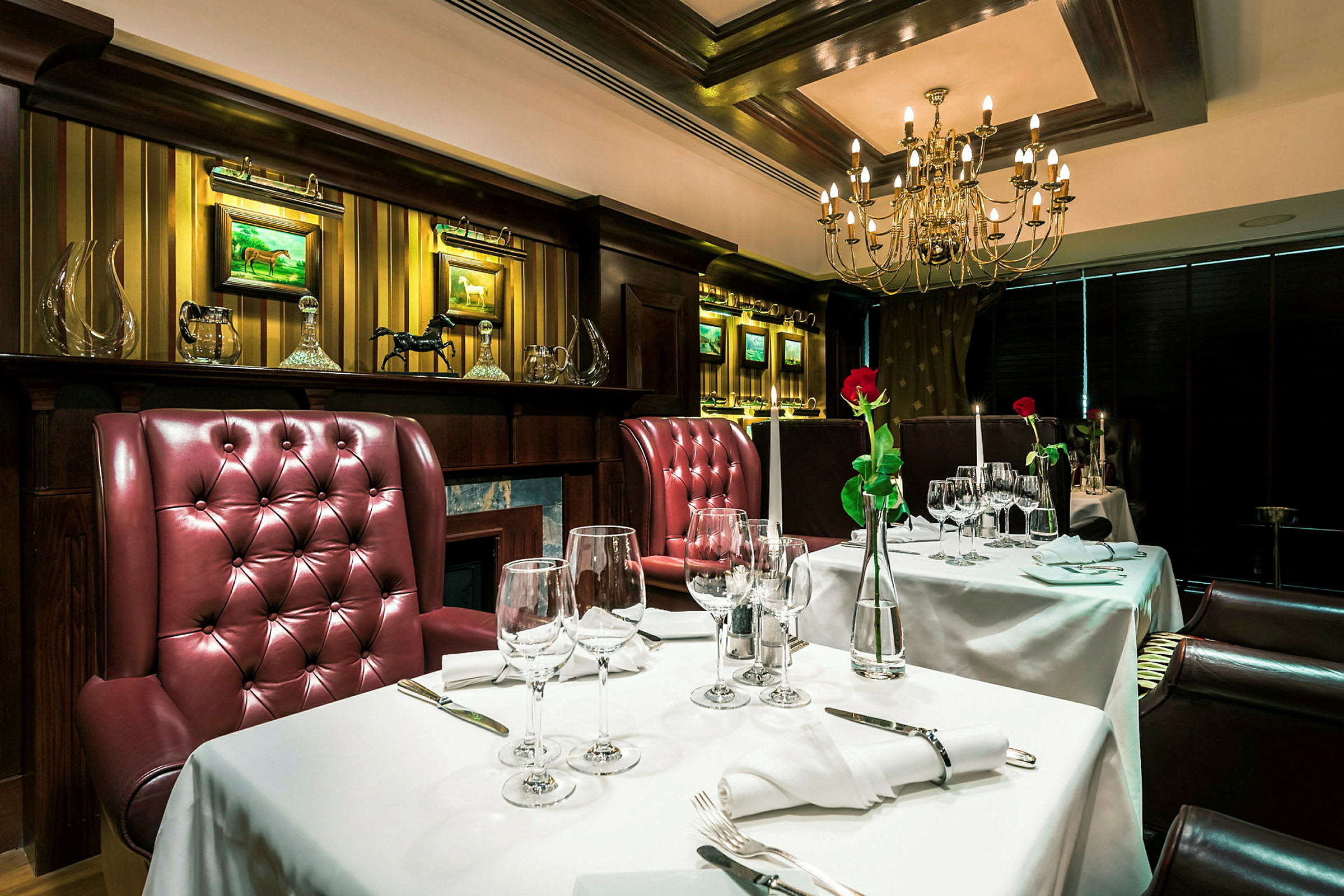 En elegant restaurantindretning med borde dækket med hvide duge, røde polstrede stole og en lysekrone i loftet. (AI-genereret tekst)