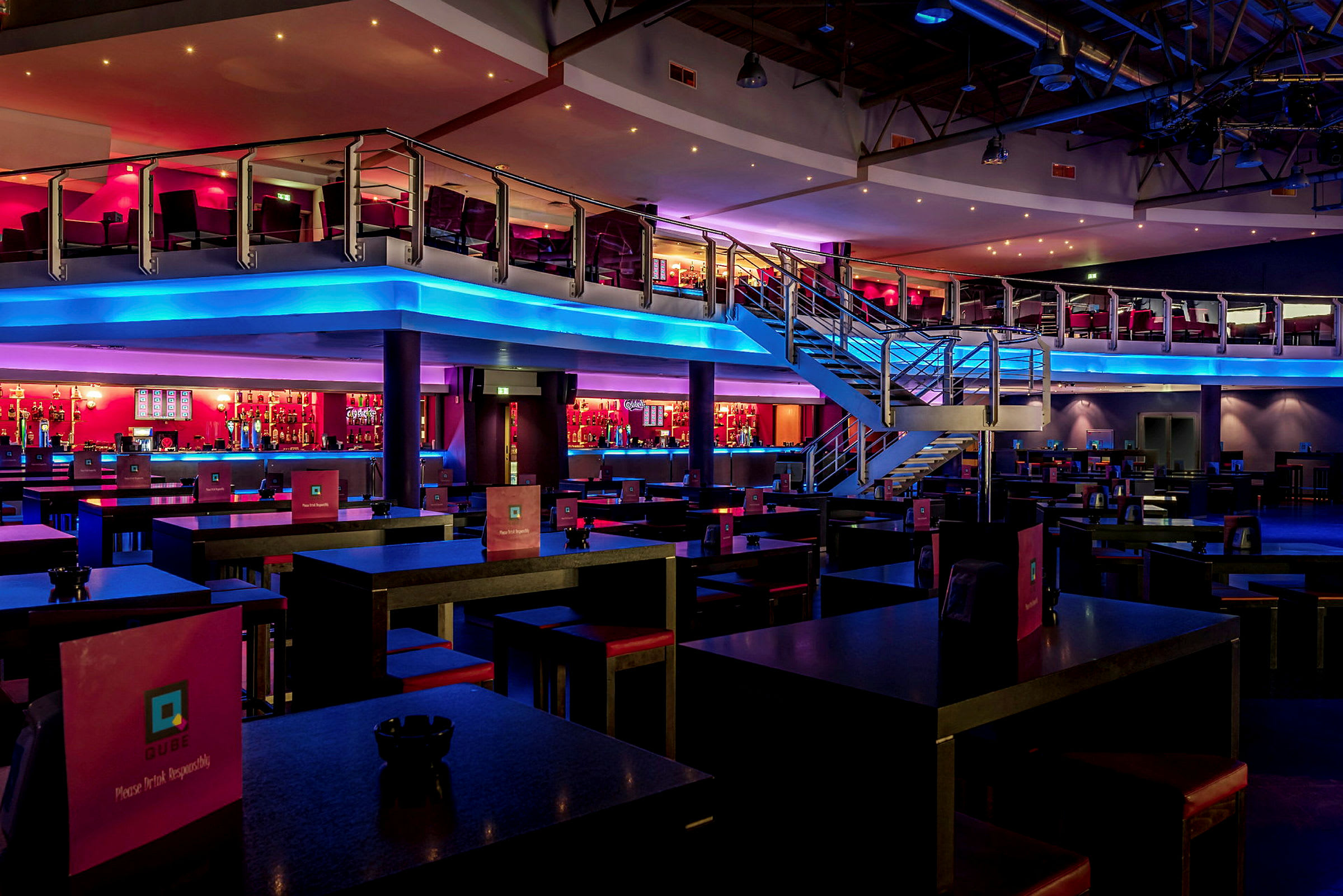 En restaurant eller natklub med et moderne interiør, to etager og farverig belysning. (AI-genereret tekst)