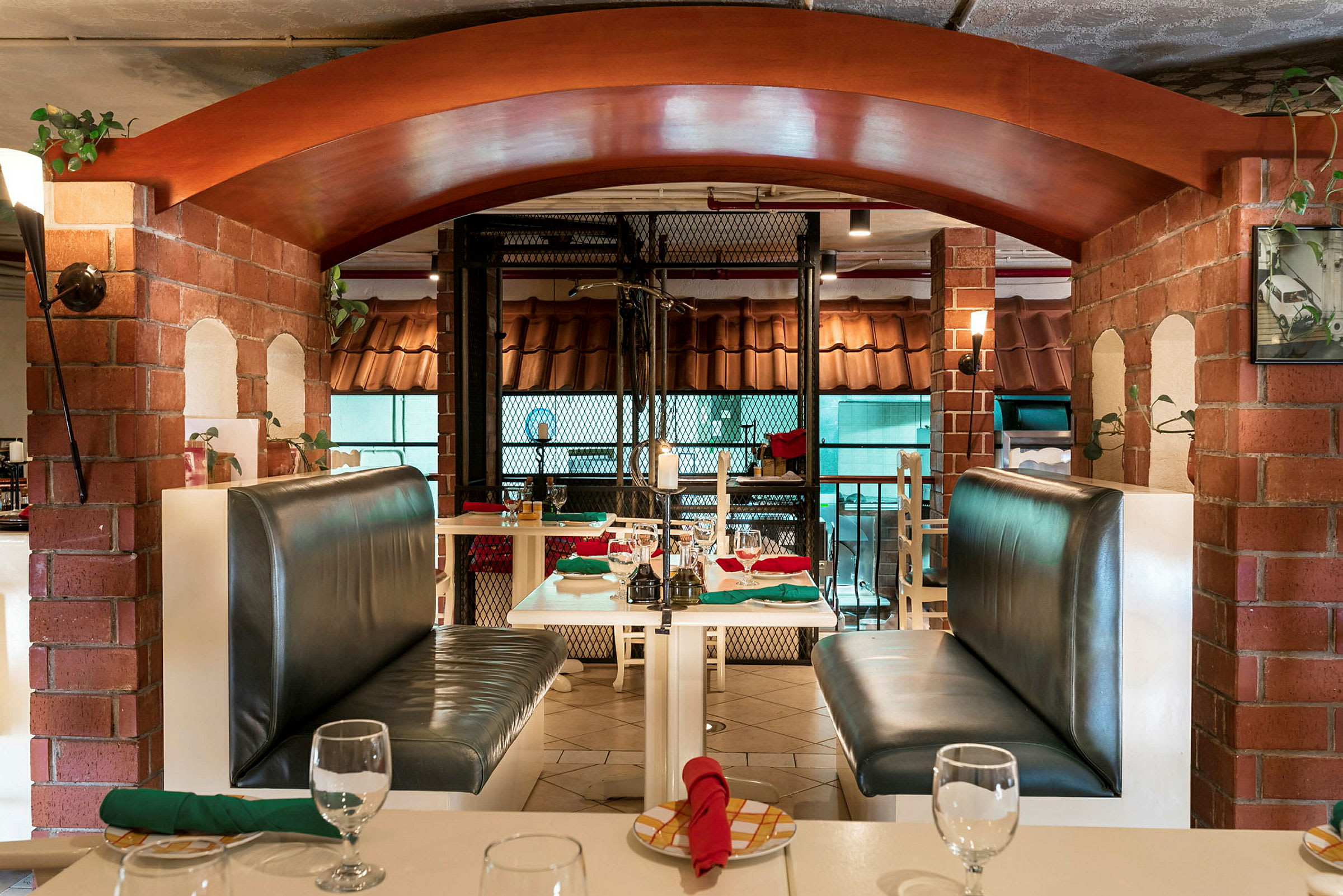 Interiør af en restaurant med borde og båse med lædersofaer samt røde og grønne servietter. (AI-genereret tekst)