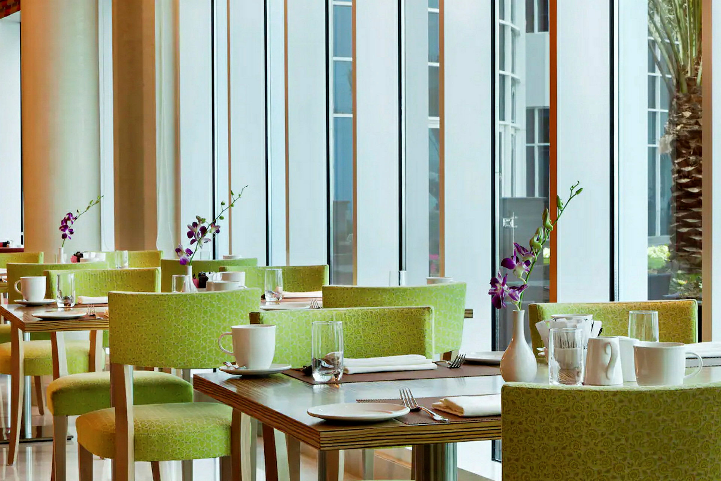 Et moderne restaurantområde med grønne stole, dækkede borde, hvide kopper og lilla orkidévaser. (AI-genereret tekst)