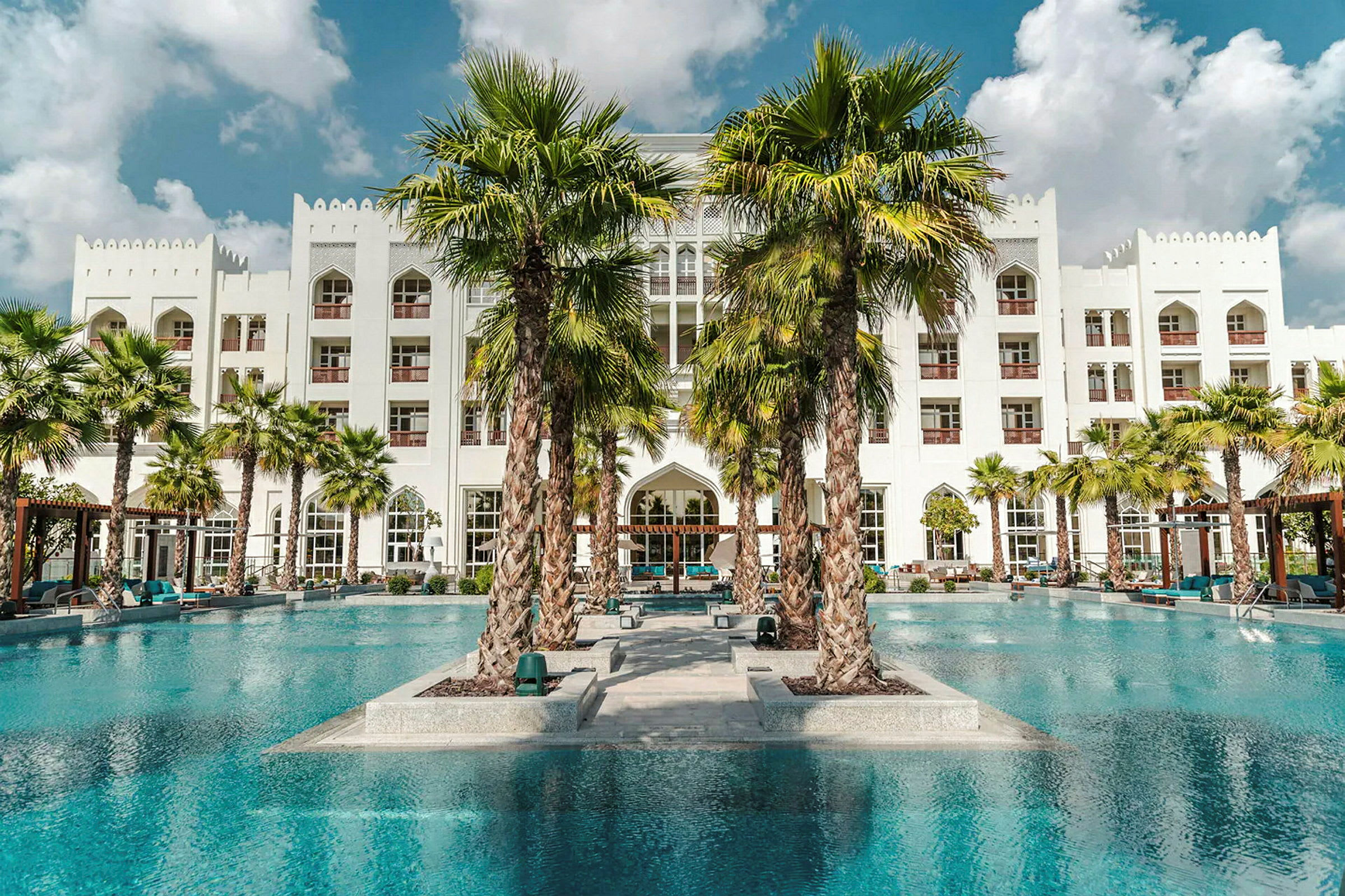 Et moderne hotel med hvid facade set fra en pool, omgivet af palmer. (AI-genereret tekst)