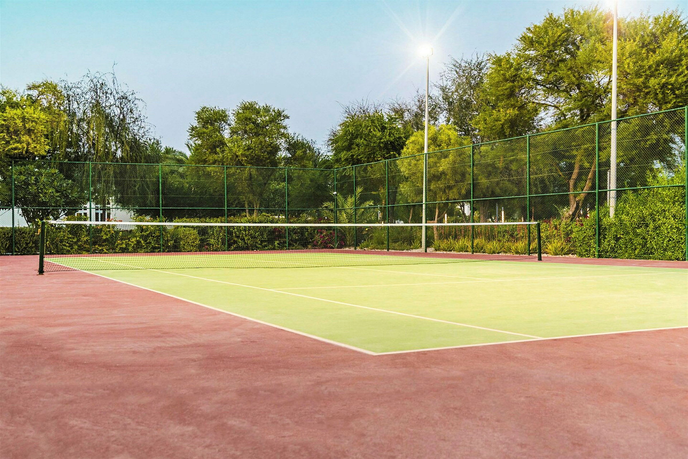 En tom tennisbane med net og omgivelser fyldt med grønt. (AI-genereret tekst)
