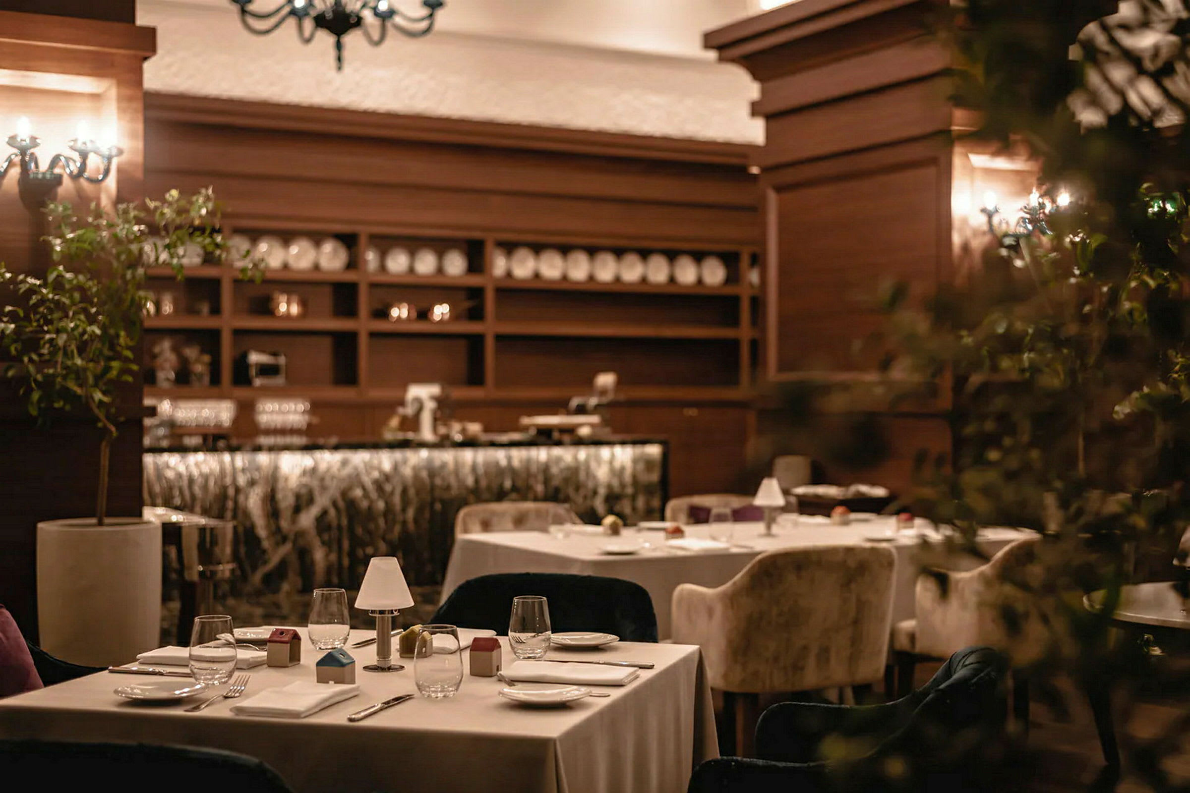 En restaurantindretning med dækkede borde og komfortable stole, omgivet af varm belysning og træudsmykning. (AI-genereret tekst)