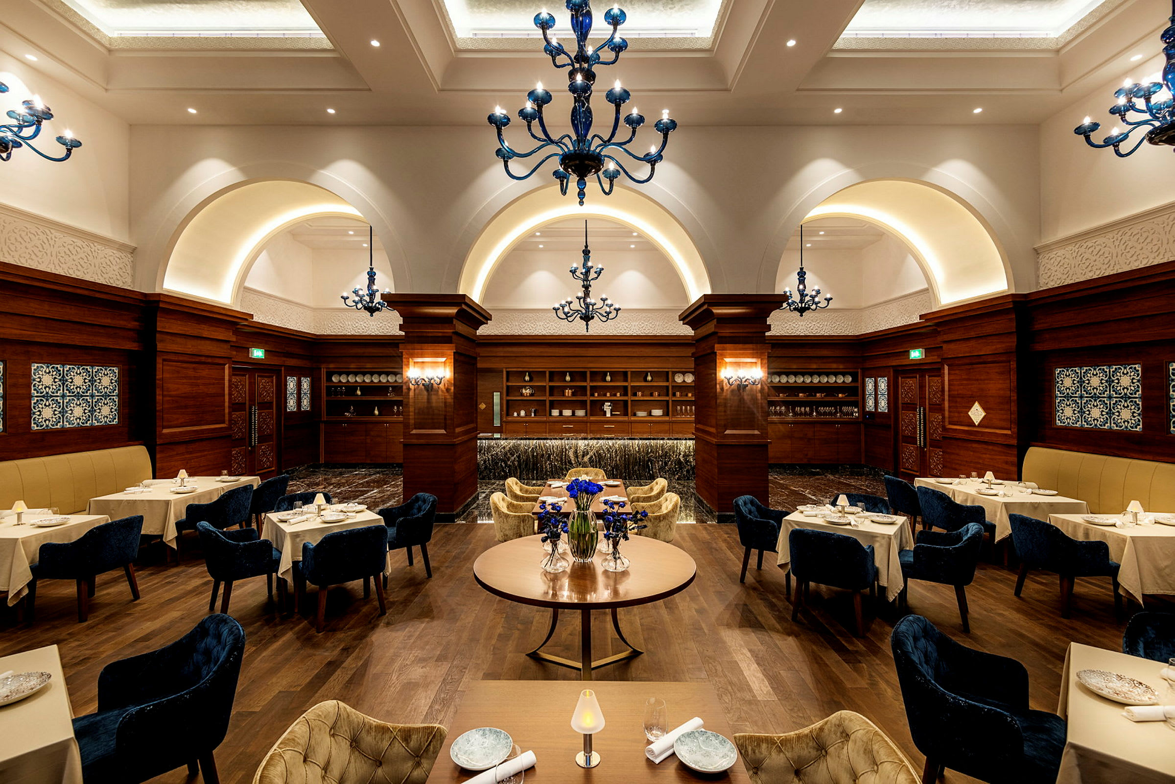 Interiør af en elegant restaurant med opdækkede borde og dekorerede blå lysekroner. (AI-genereret tekst)