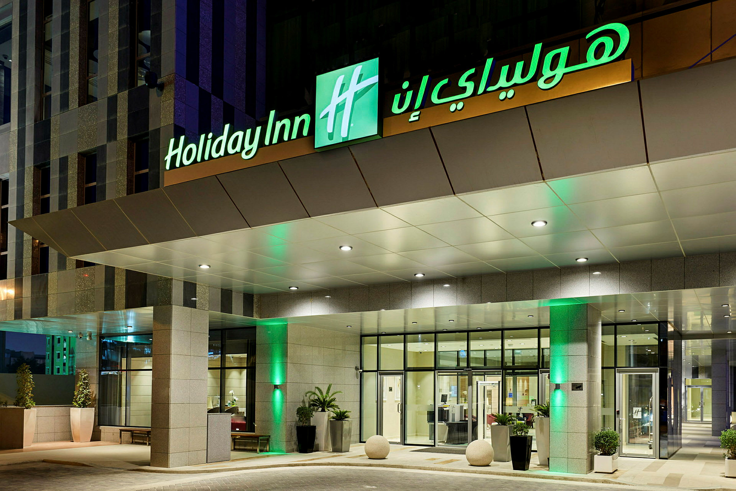 Indgangen til et hotel med skiltet 'Holiday Inn' oplyst. (AI-genereret tekst)