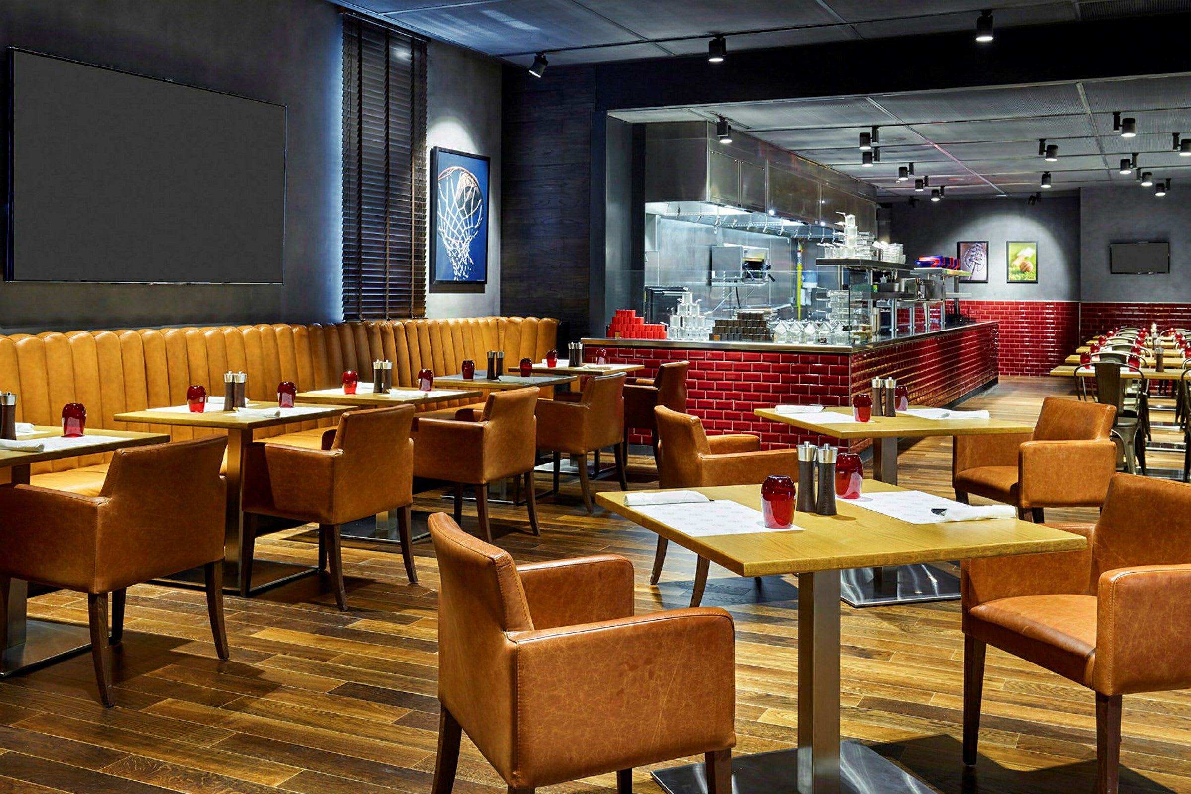 En moderne restaurant med træborde og komfortable læderstole. Væggene er dekorerede med kunst og et åbent køkken med røde fliser. (AI-genereret tekst)