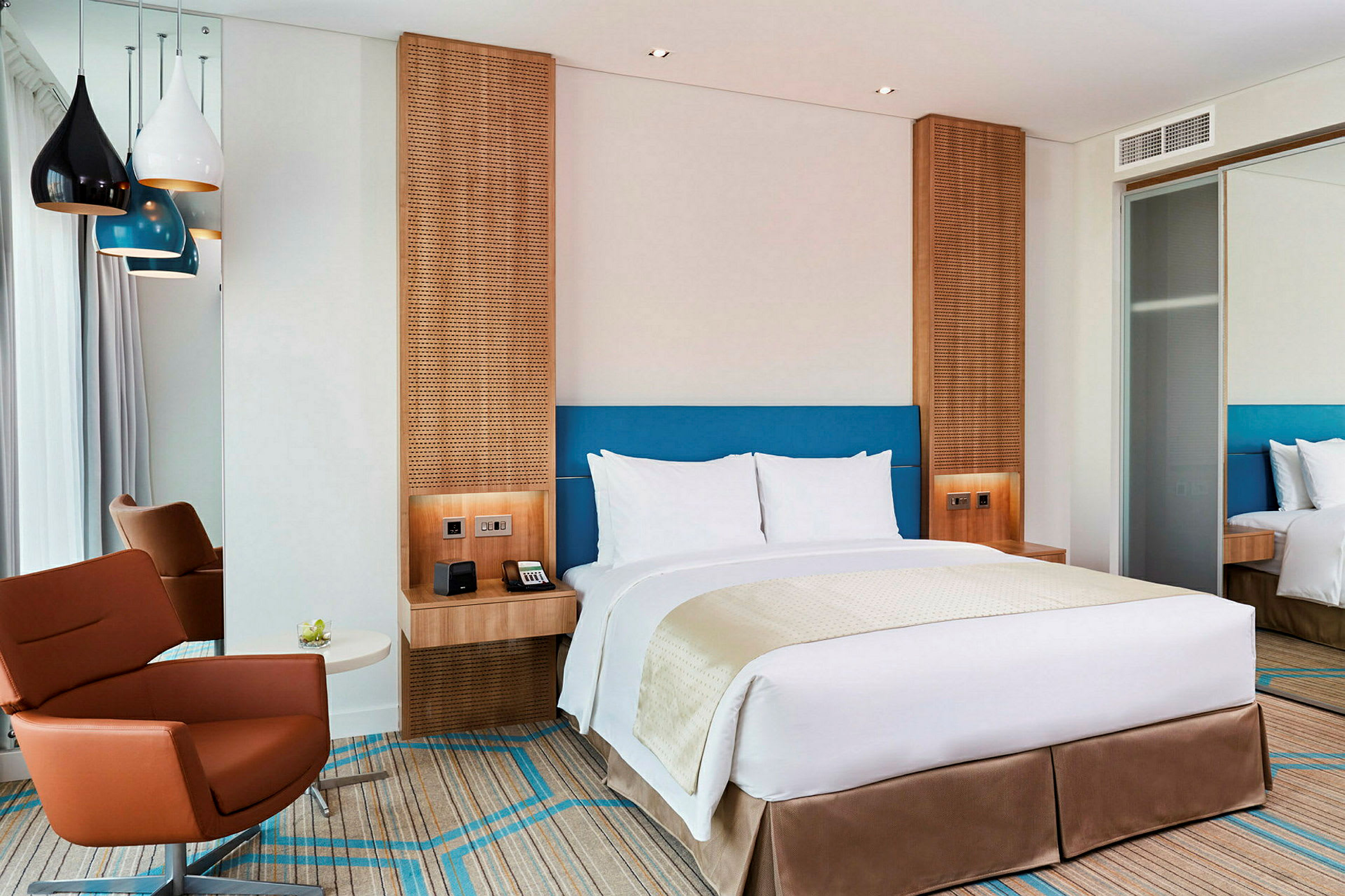 Et moderne hotelværelse med en dobbeltseng, en brun lænestol og farverige lamper, der hænger fra loftet. (AI-genereret tekst)