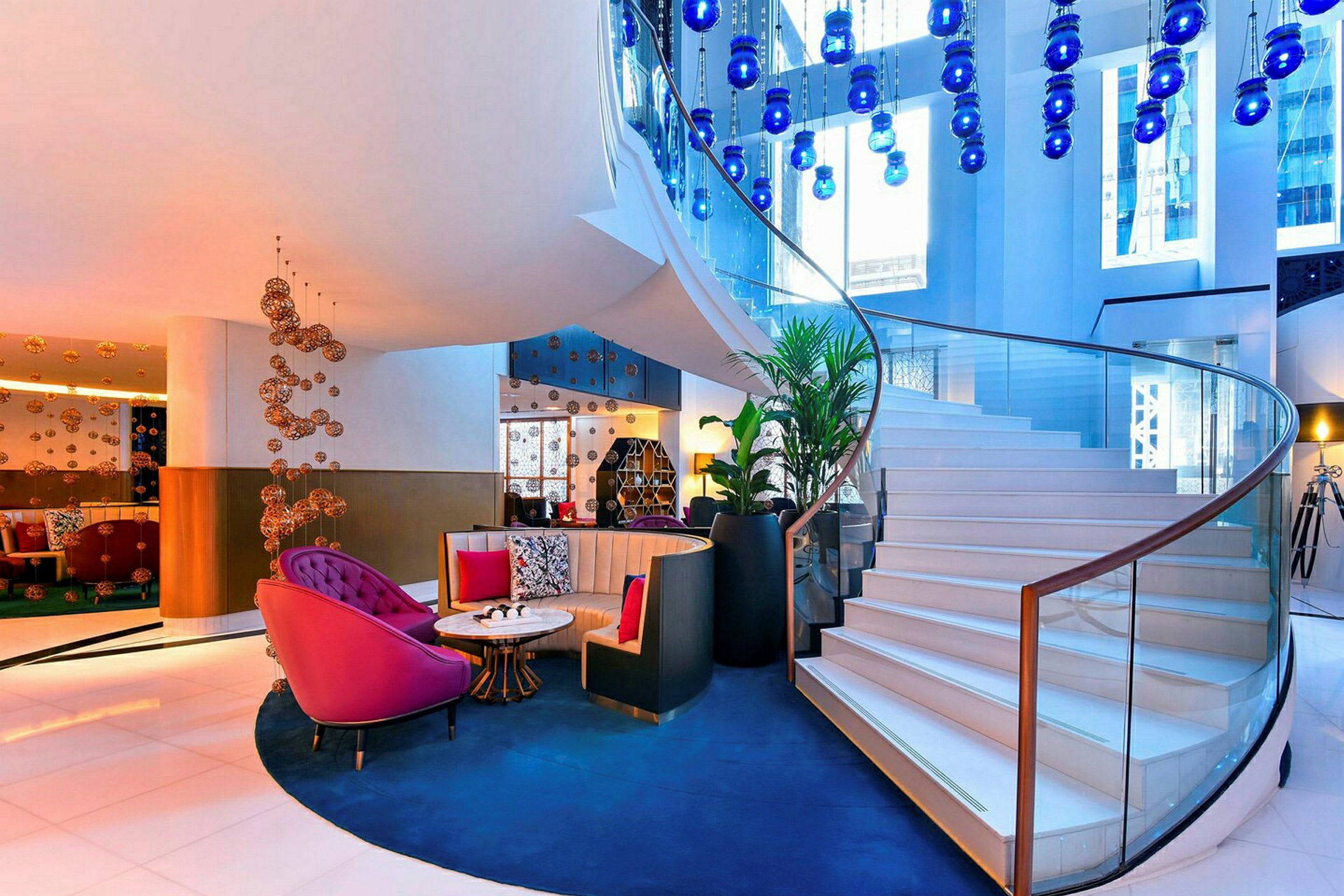 Lys og elegant hotellobby med vindeltrappe og dekorative blå lamper. (AI-genereret tekst)