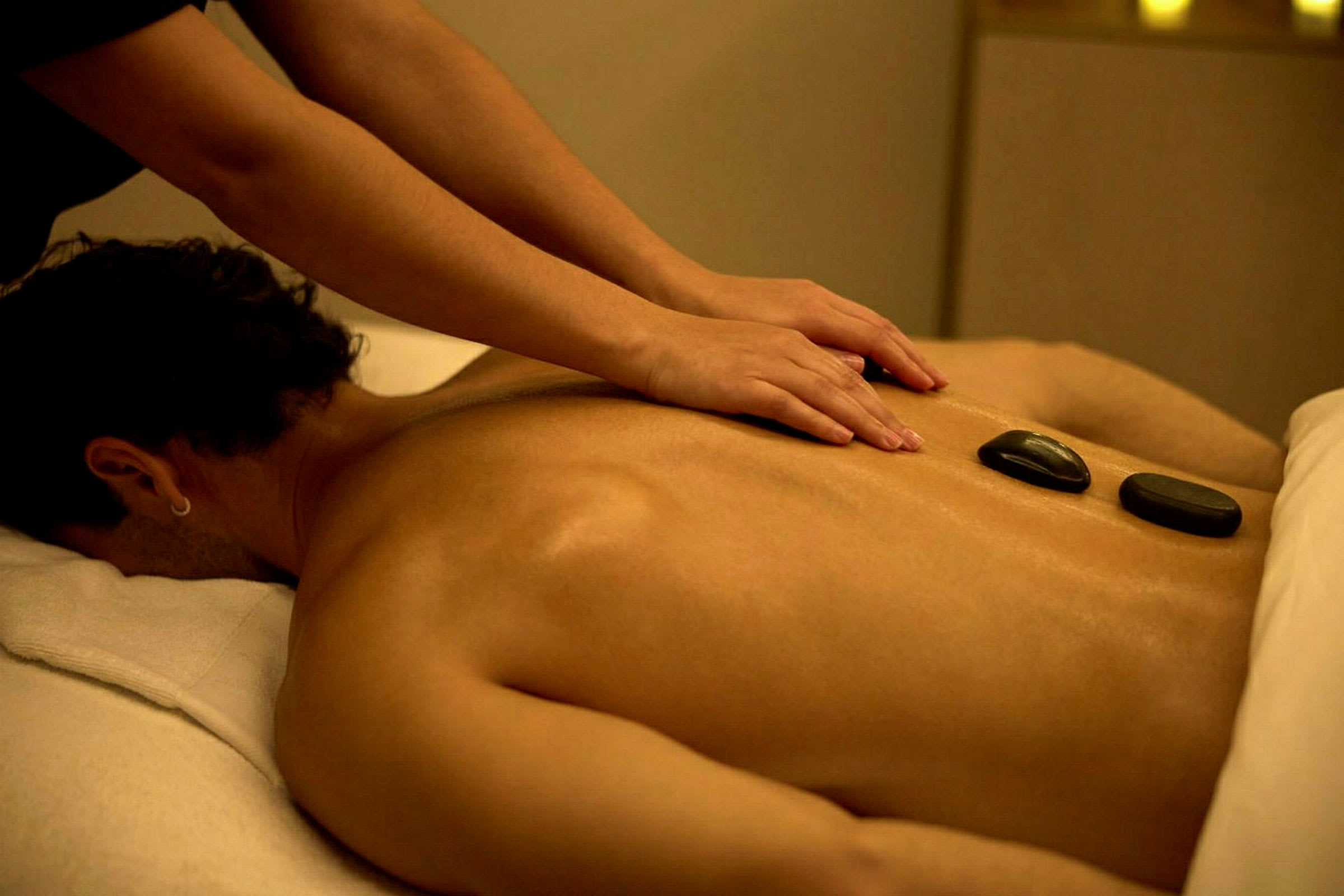 En person får massage på ryggen med to varme sten placeret. (AI-genereret tekst)