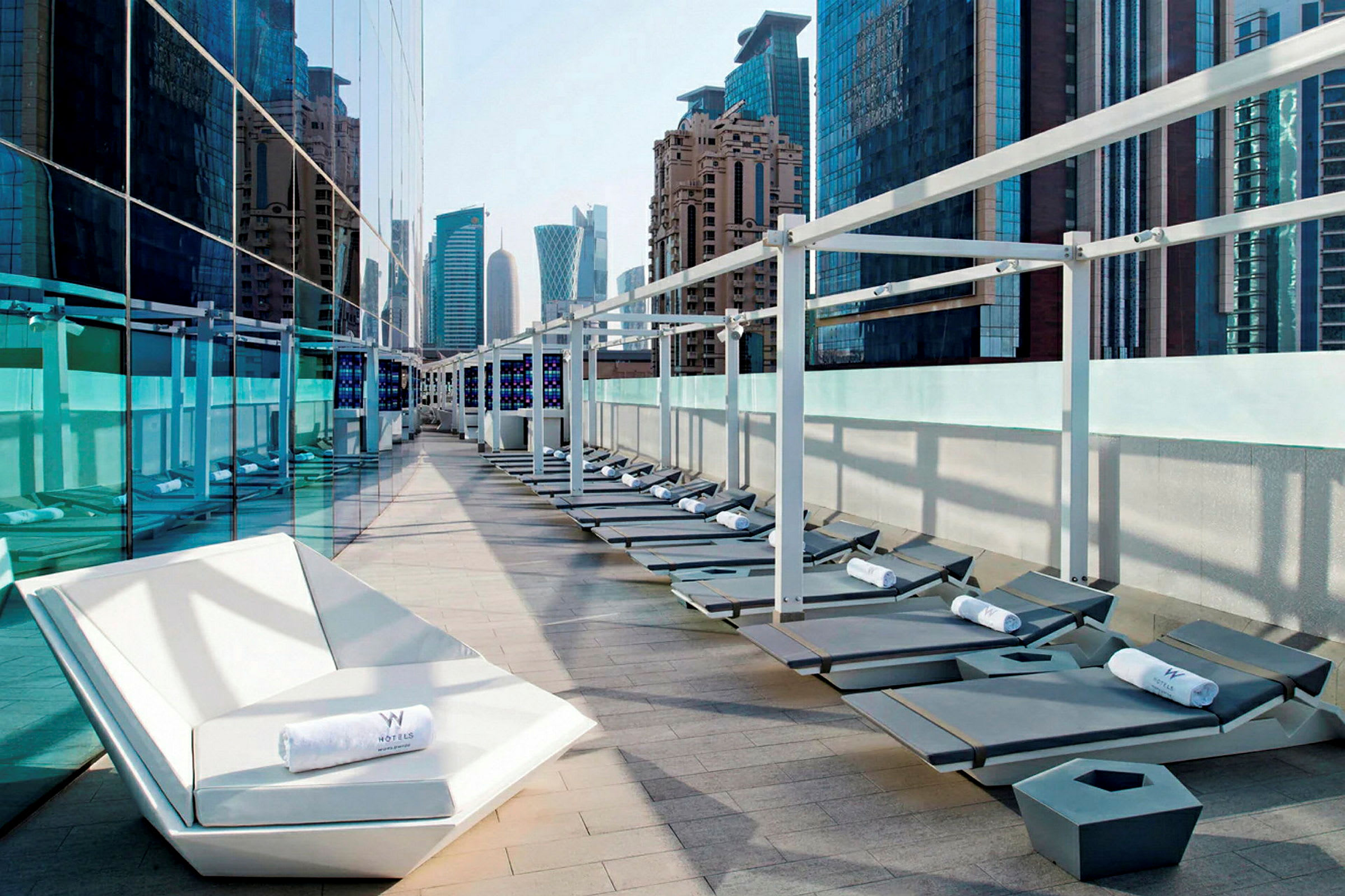 Liggestole og en lounge på en terrasse med udsigt til moderne bygninger. (AI-genereret tekst)