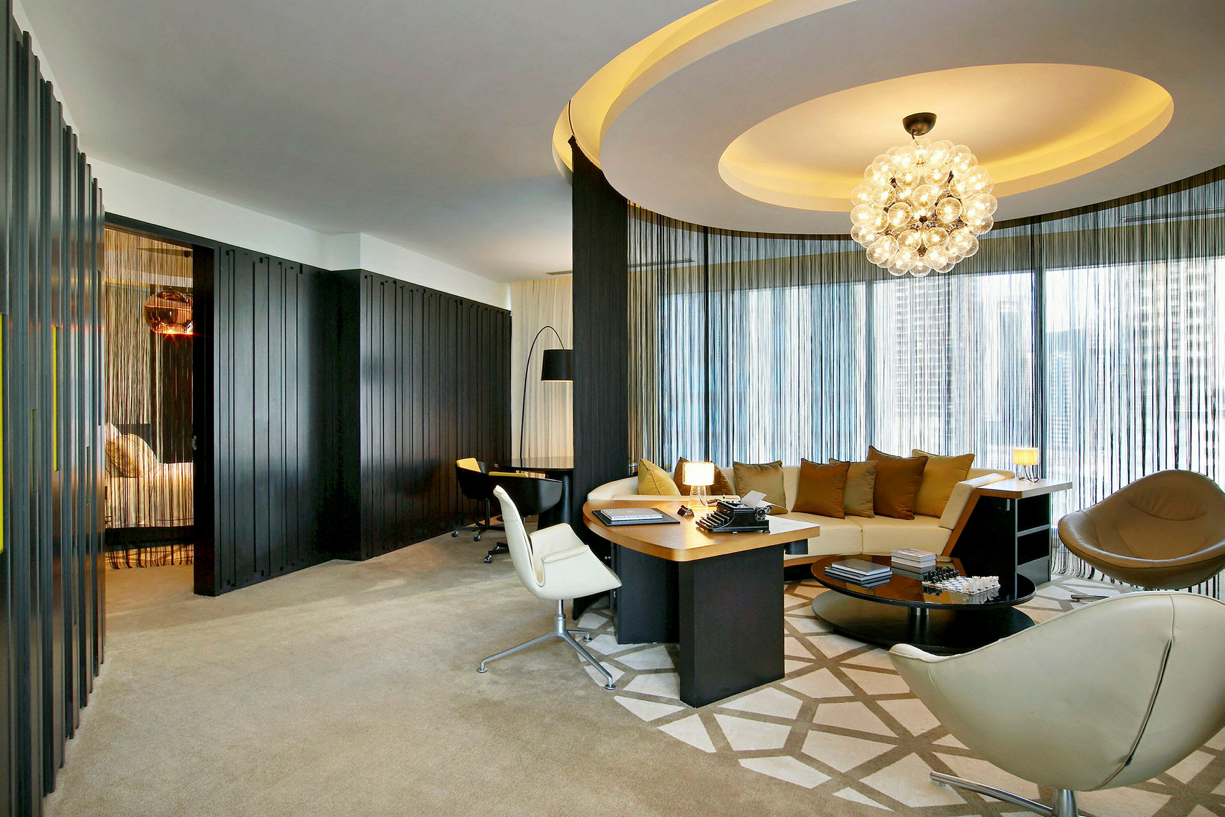 Et elegant hotelværelse med moderne møblering, herunder en rund sofa, skrivebord og dekorativ belysning. (AI-genereret tekst)