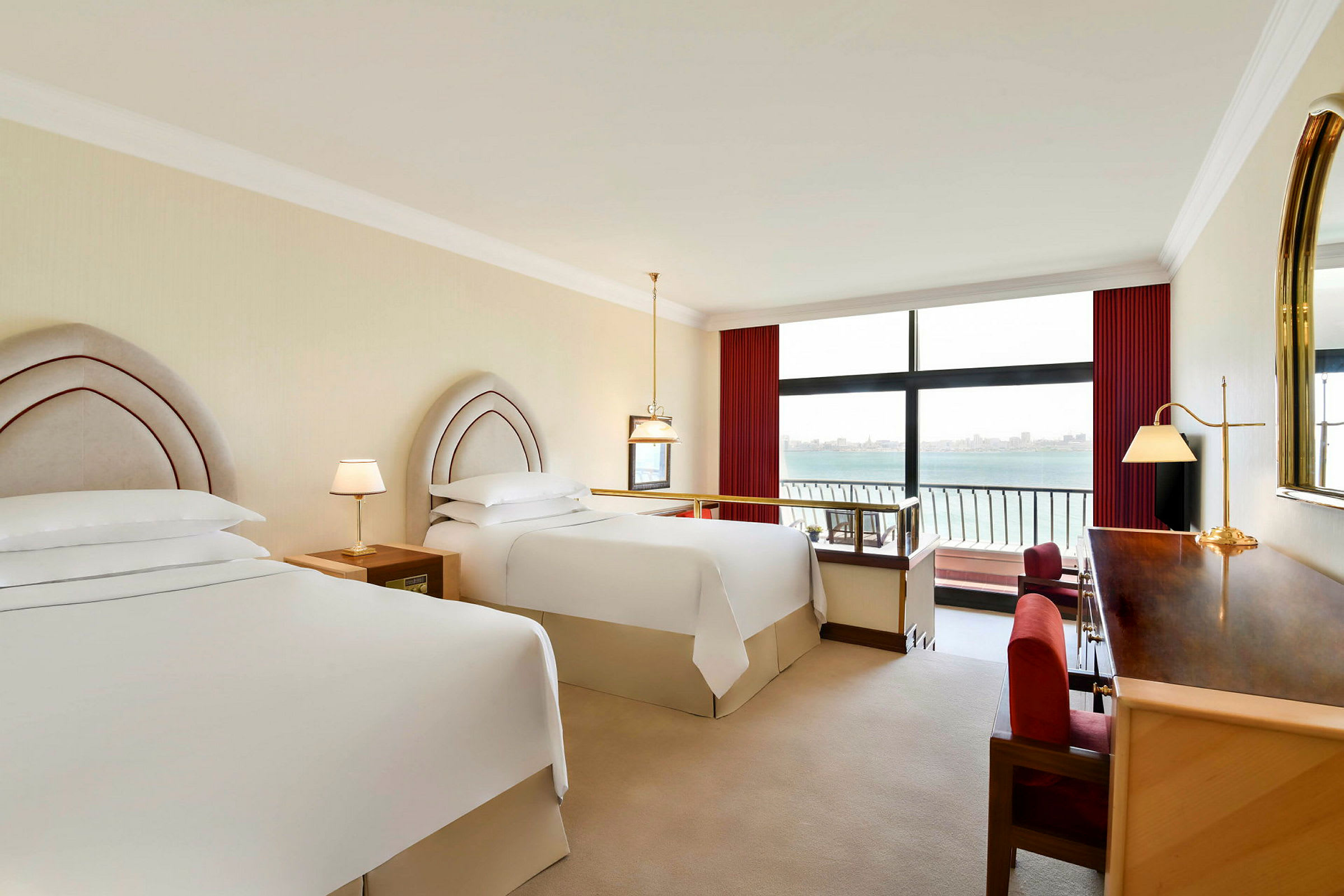 Hotelværelse med to senge ved siden af et stort vindue med udsigt over havet. (AI-genereret tekst)