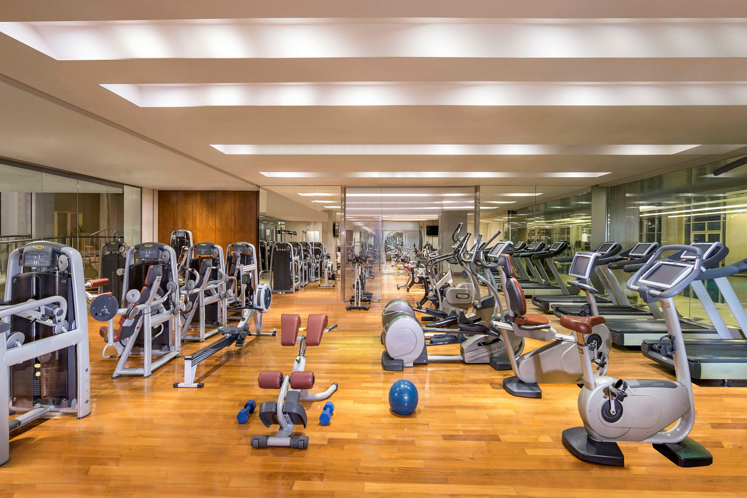 Et fitnesscenter med træningsmaskiner, løbebånd, motionscykler og frie vægte på et trægulv. (AI-genereret tekst)