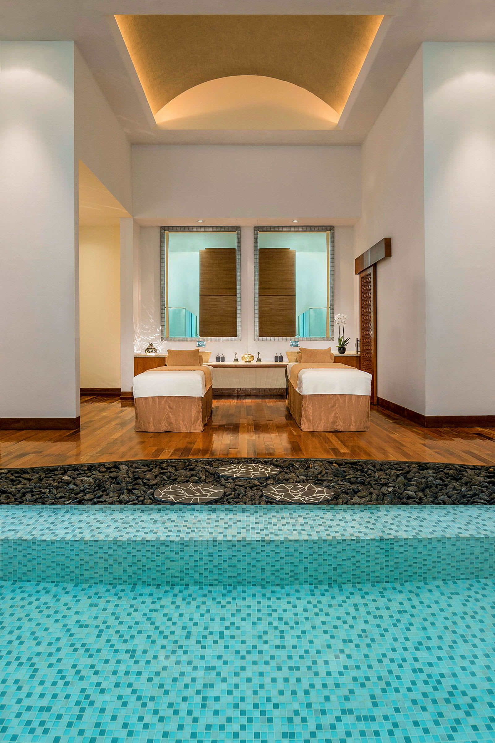 Et elegant spa med trægulv, to massagebænke og en pool med turkise mosaikfliser. (AI-genereret tekst)