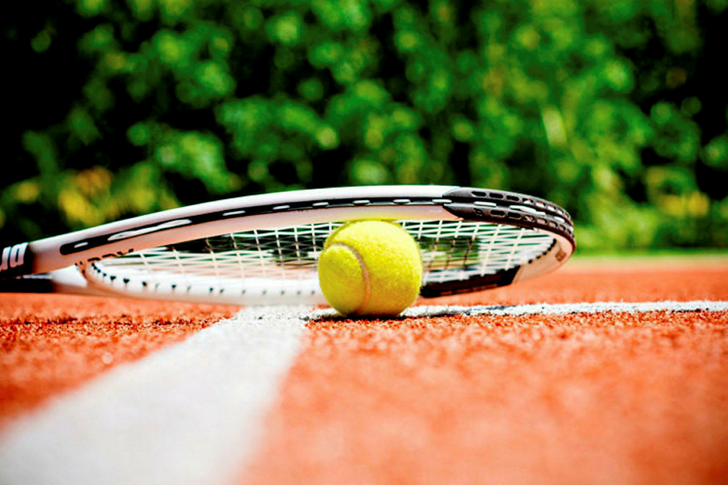 En tennisbold og en ketsjer ligger på en rød tennisbane nær en hvid linje. (AI-genereret tekst)